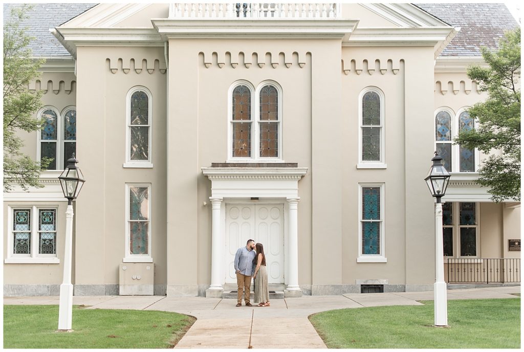 engaged couple kissing in front of white doors of moravian church building in downtown lititz pennsylvania