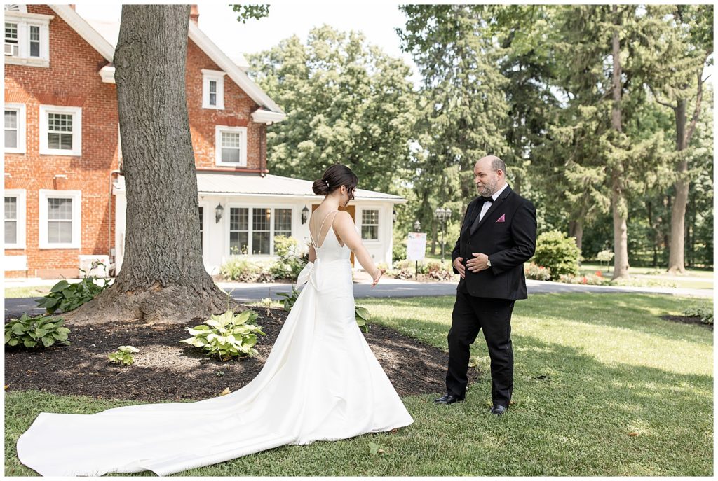 bride sharing a first look moment outdoors with her father by house at cameron estate inn