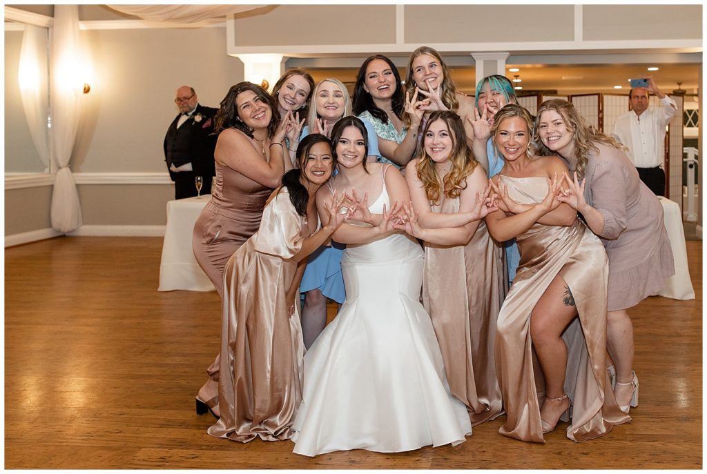 bride and a large group of her female friends all huddled together and smiling at camera during reception at cameron estate inn
