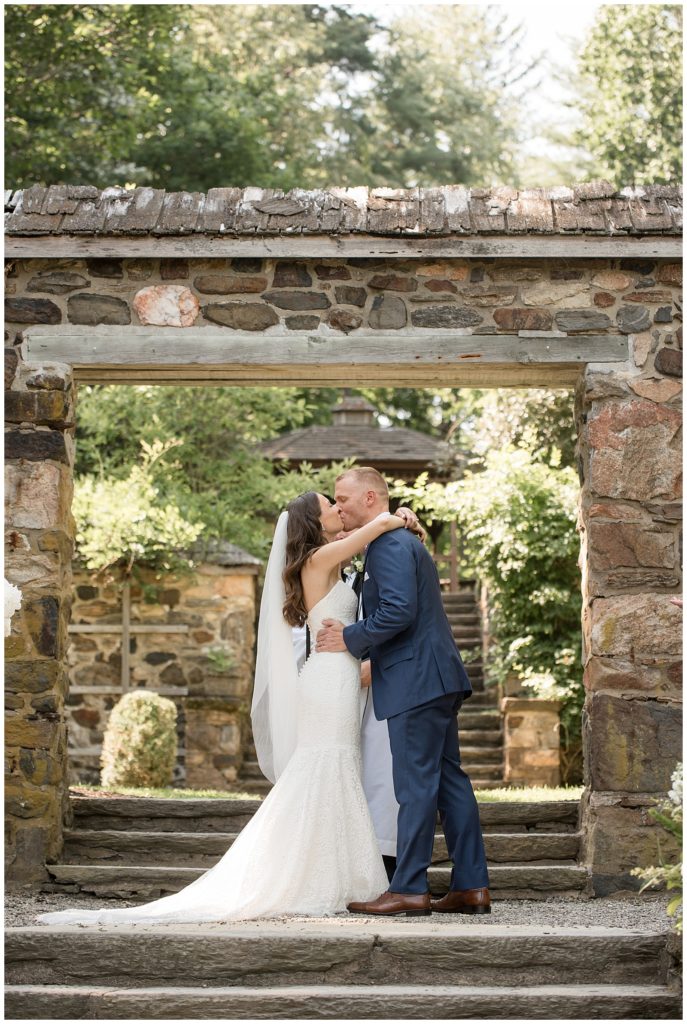bride and groom kissing under stone archway at outdoor wedding ceremony at parque ridley creek