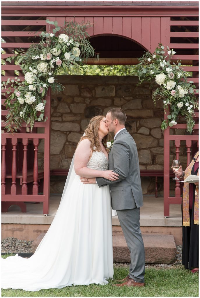 bride and groom kissing by maroon arbor with beautiful florals at elizabeth furnace