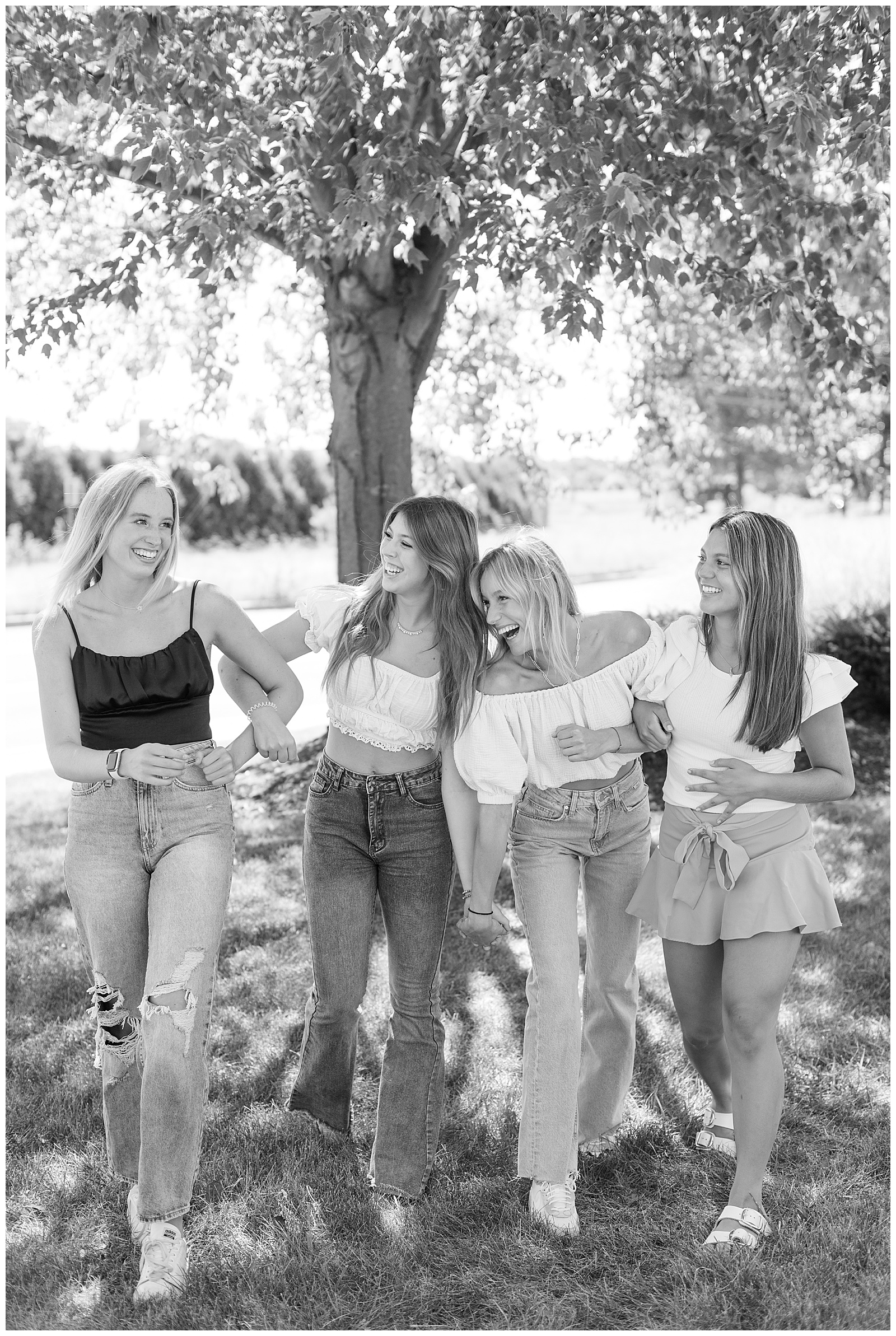 black and white photo of four senior girls with arms linked being silly by trees in lancaster pennsylvania