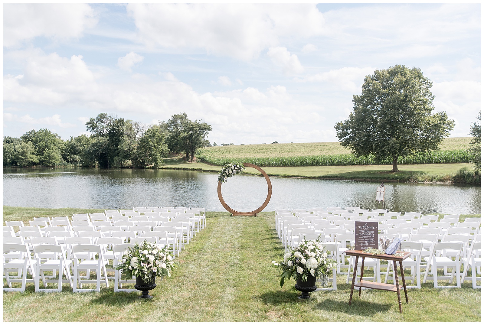 rows of white chairs facing lake with round wooden display along lake before wedding ceremony at lakefield weddings