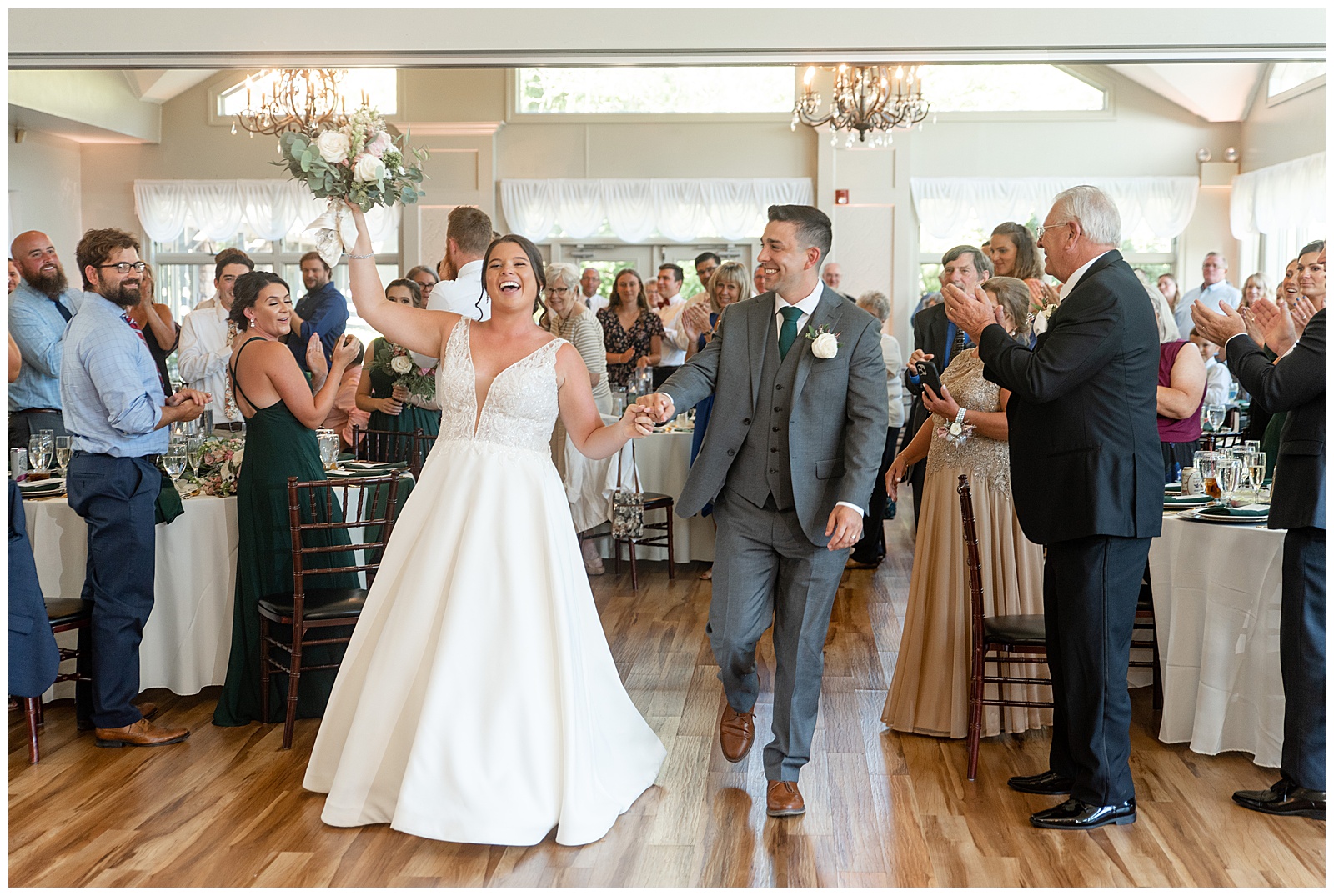 bride raising her bouquet overhead and holding hands with her groom as they enter reception at the manor at mountain view