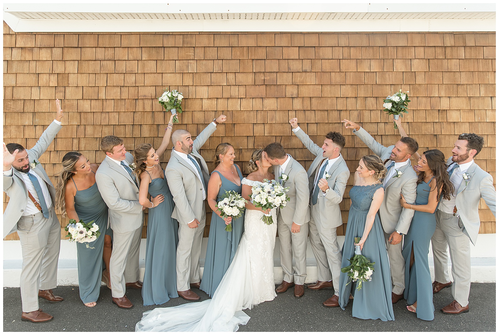 couple kissing as their bridal party cheers for them and raises bouquets in the air at venue in bay shore new york