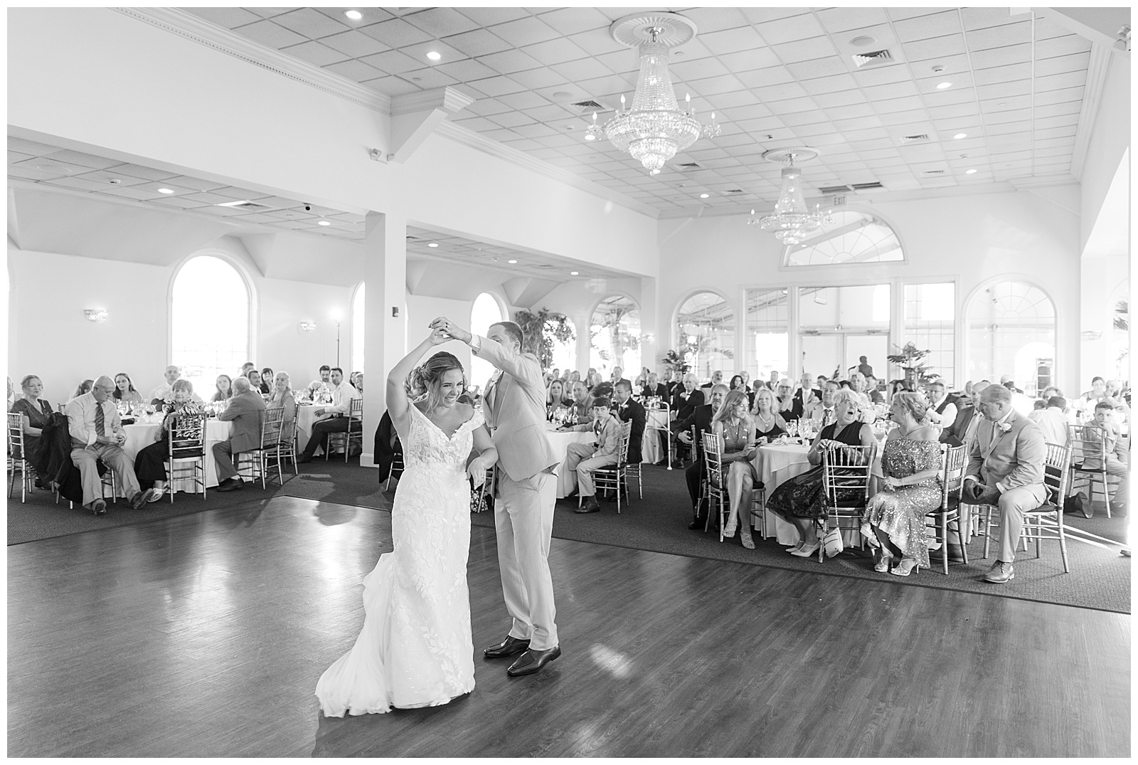 black and white photo of groom twirling his bride during their first dance inside reception at captain bill's