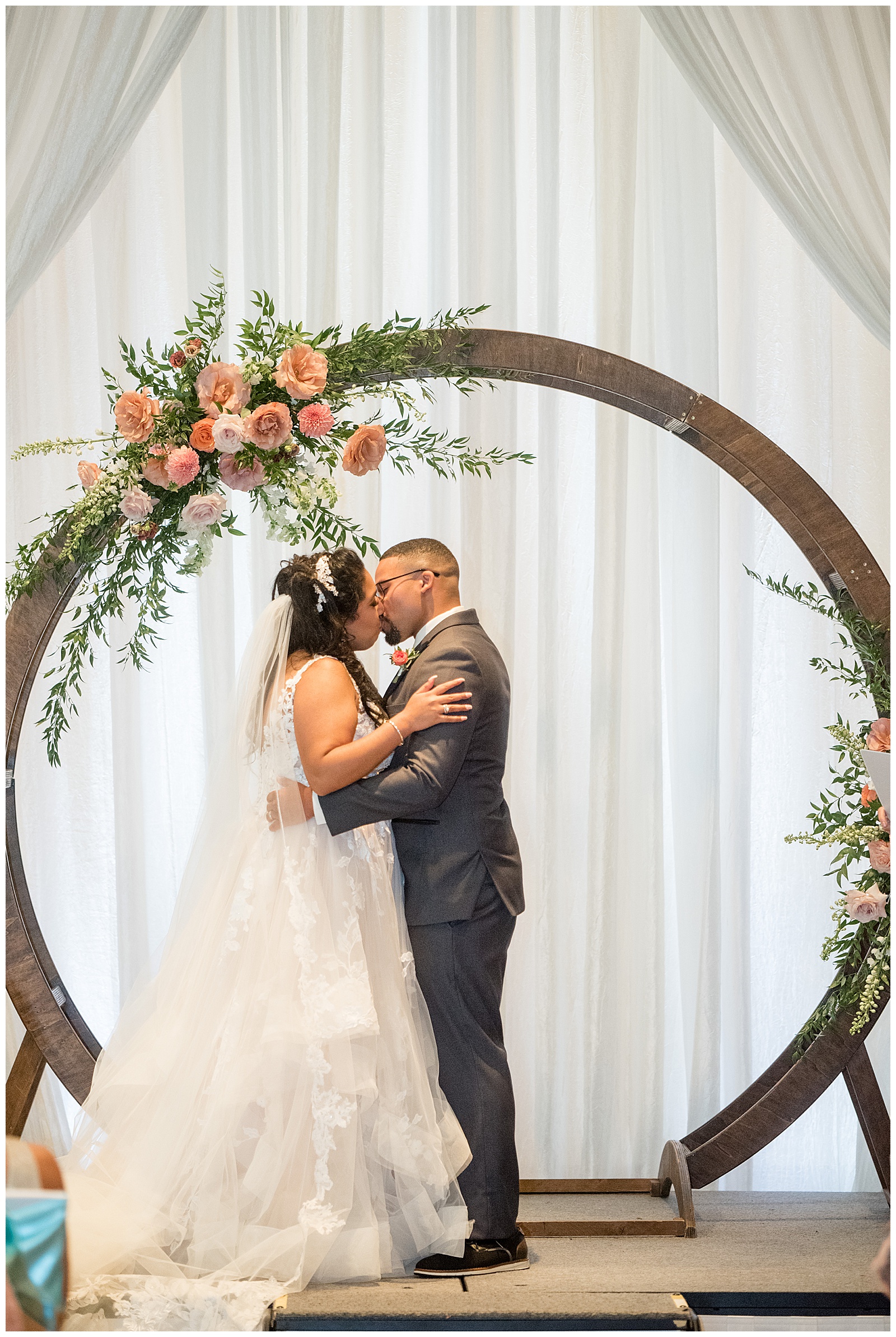bride and groom share their first kiss during wedding ceremony inside the lancaster marriott in penn square by wooden and floral display