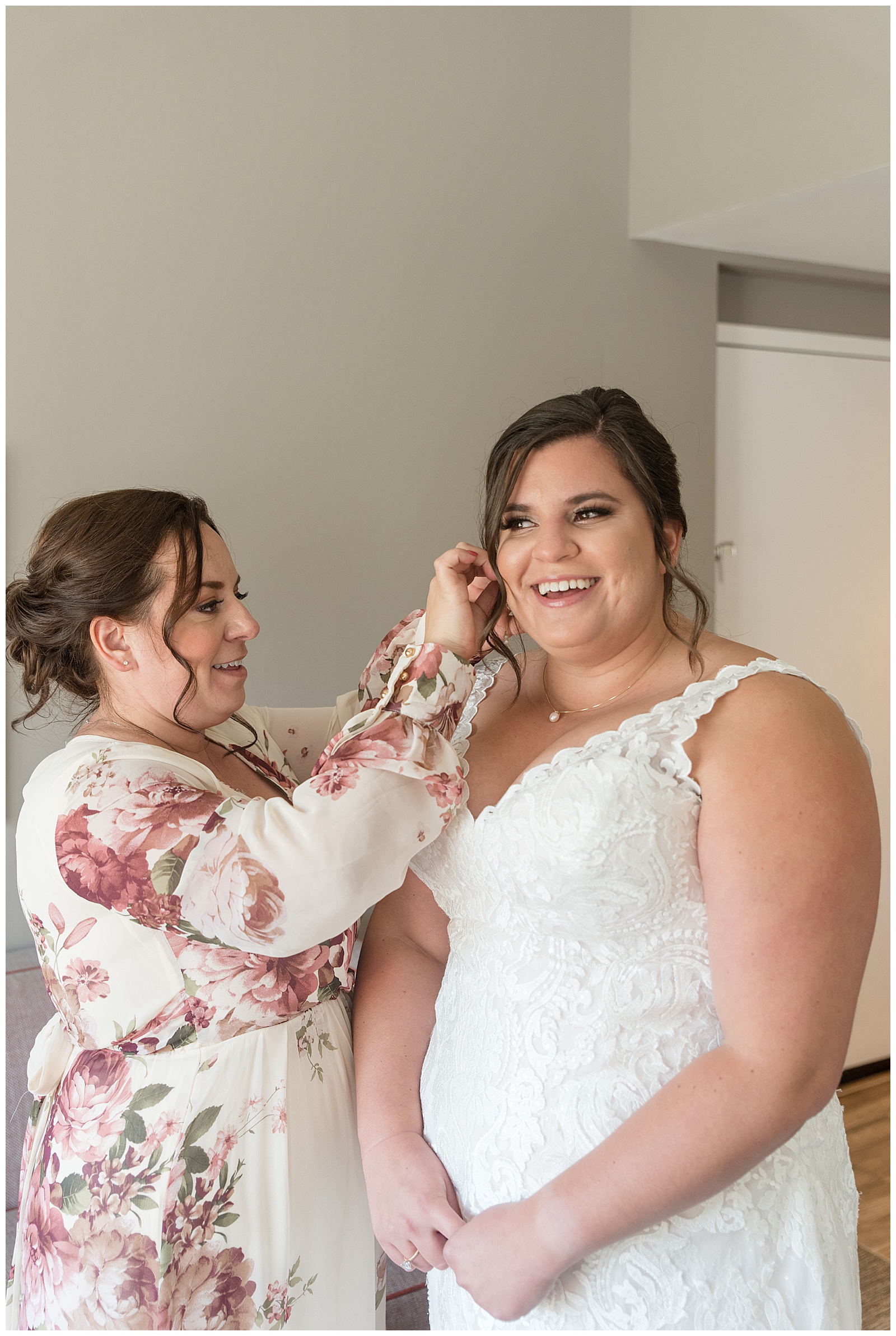 maid of honor helping bride with her right earring as they both smile in bridal suite at folino estate