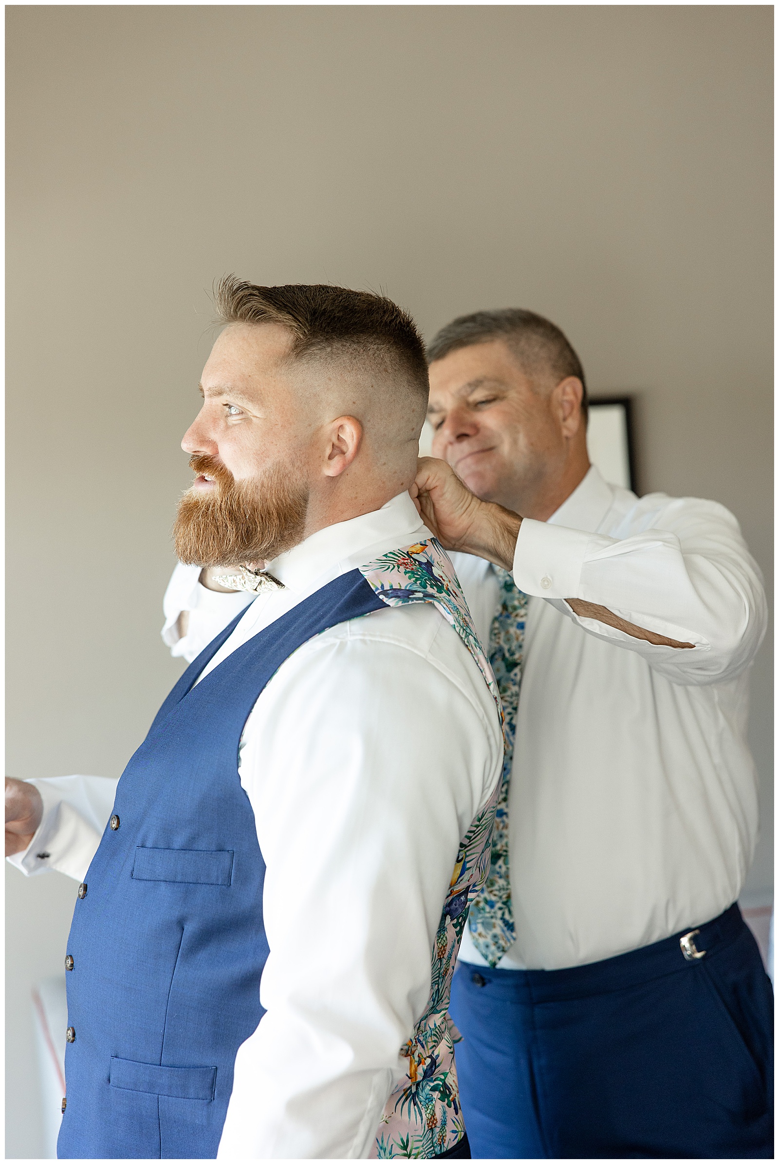 best man helping groom with his collar as groom faces right in suite at folino estate