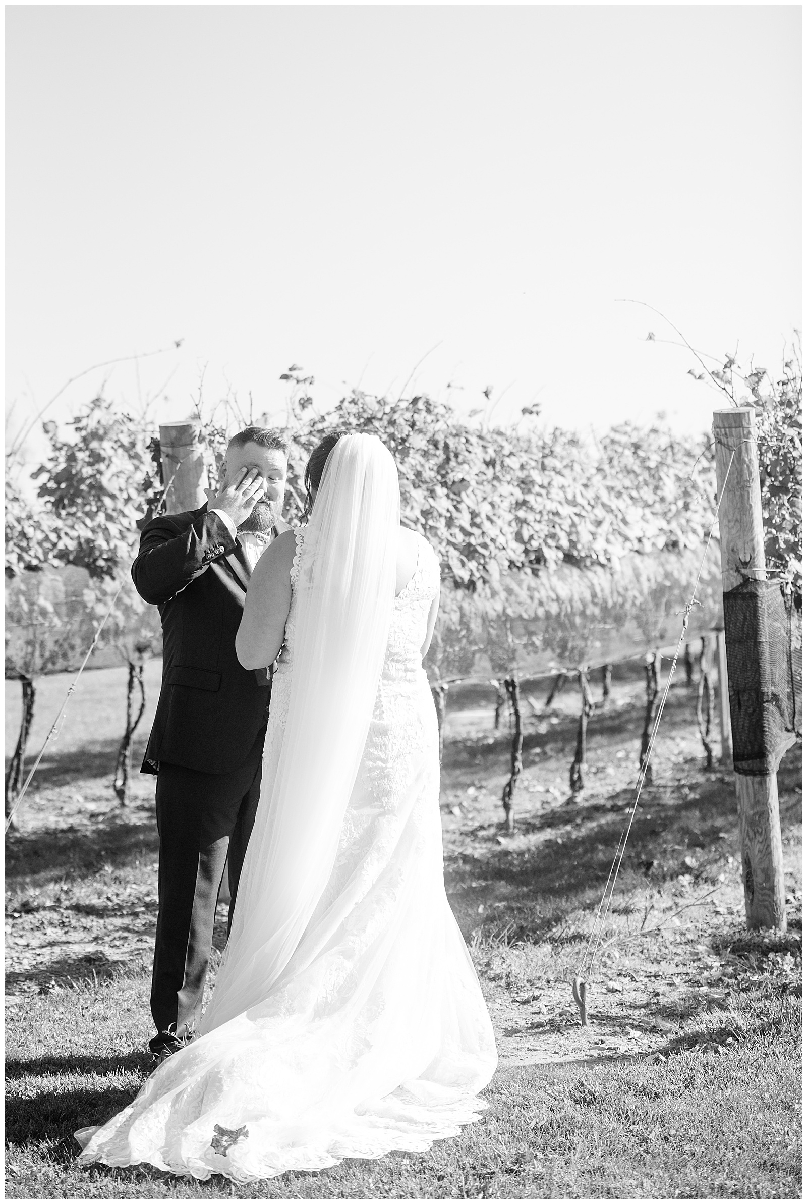 black and white photo of first look moment with bride and groom as groom wipes away tears in vineyard at folino estate