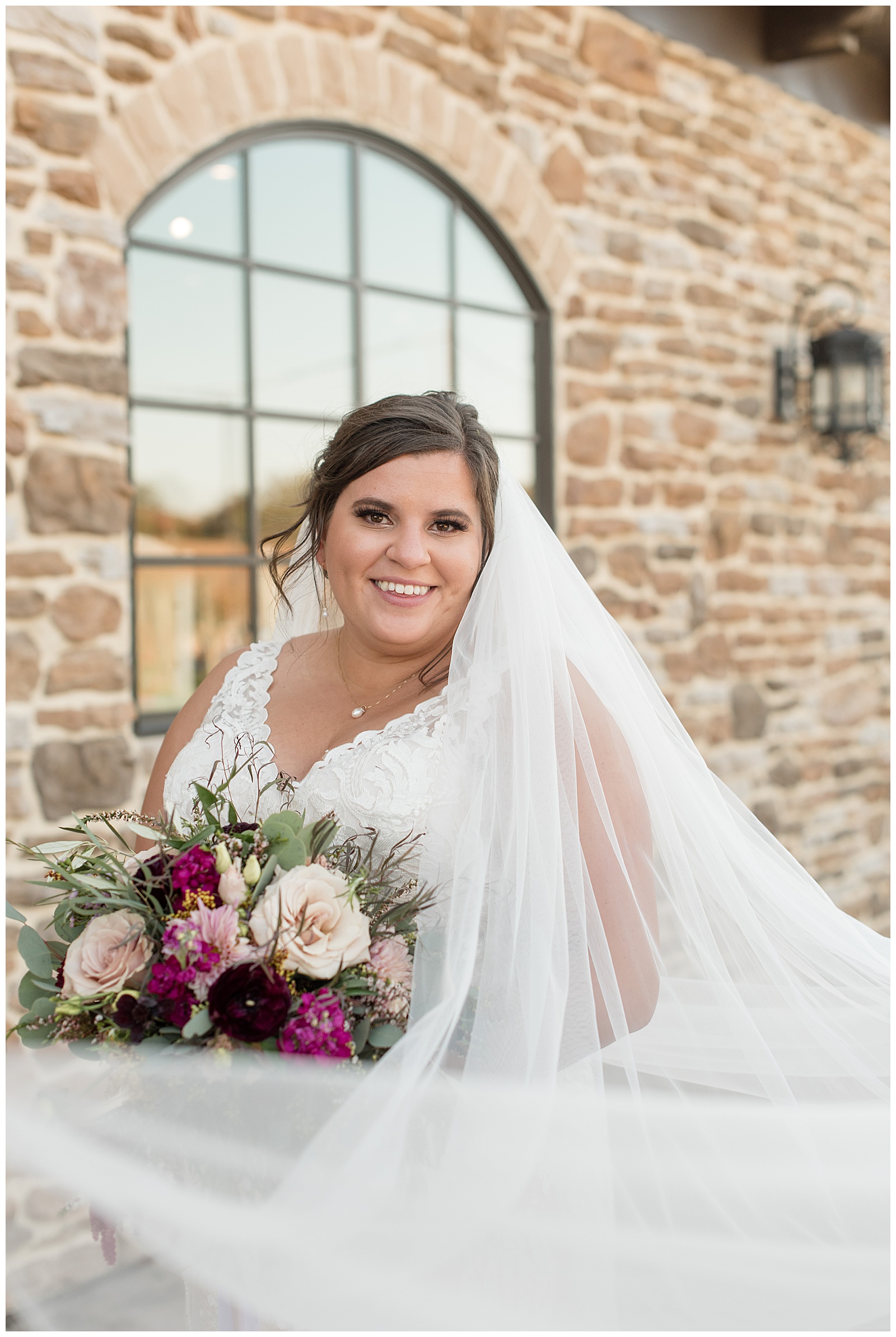 closeup photo of bride smiling with her veil over her left shoulder holding maroon and pink bouquet at folino estate