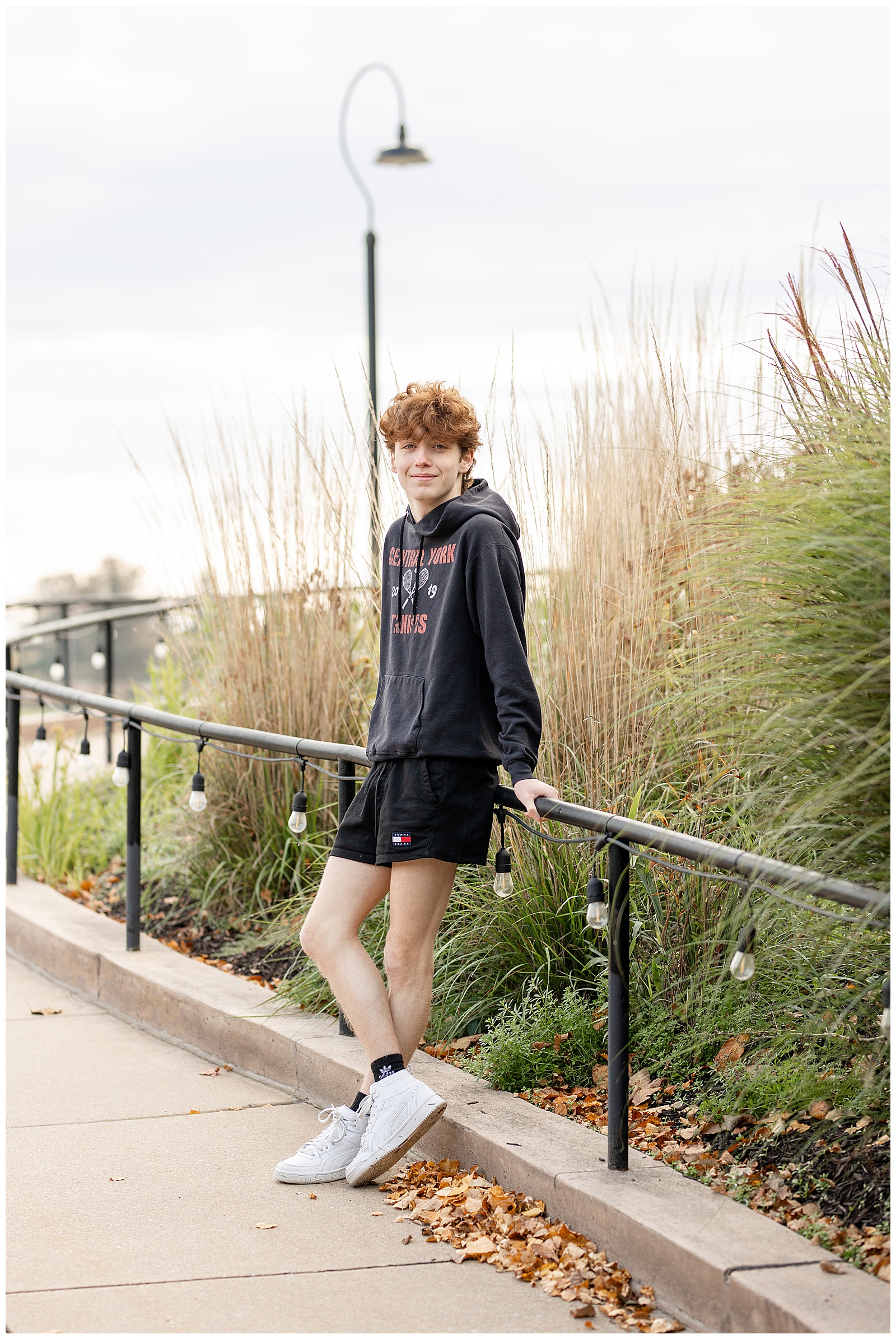 senior guy wearing central york tennis hoodie and black shorts and leaning against railing at overlook park
