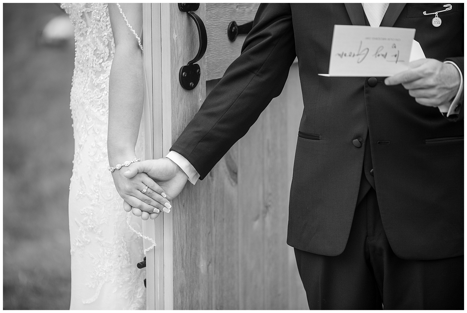 close up black and white photo of bride and groom holding hands with door between them at stoltzfus homestead and gardens