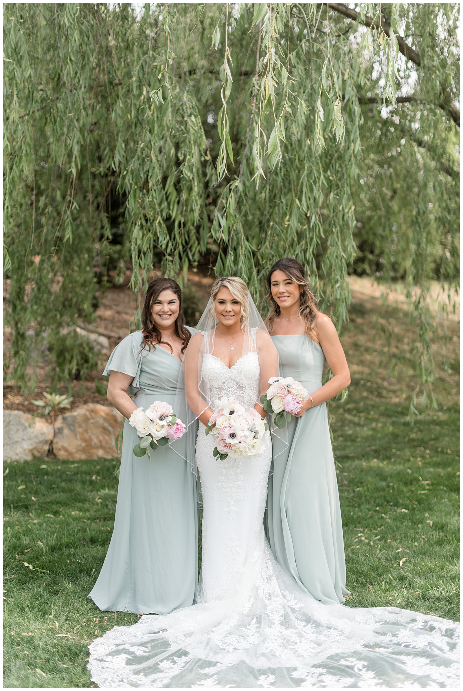 bride with two of her maids of honor holding bouquets under willow tree at barn wedding venue in lancaster county pennsylvania
