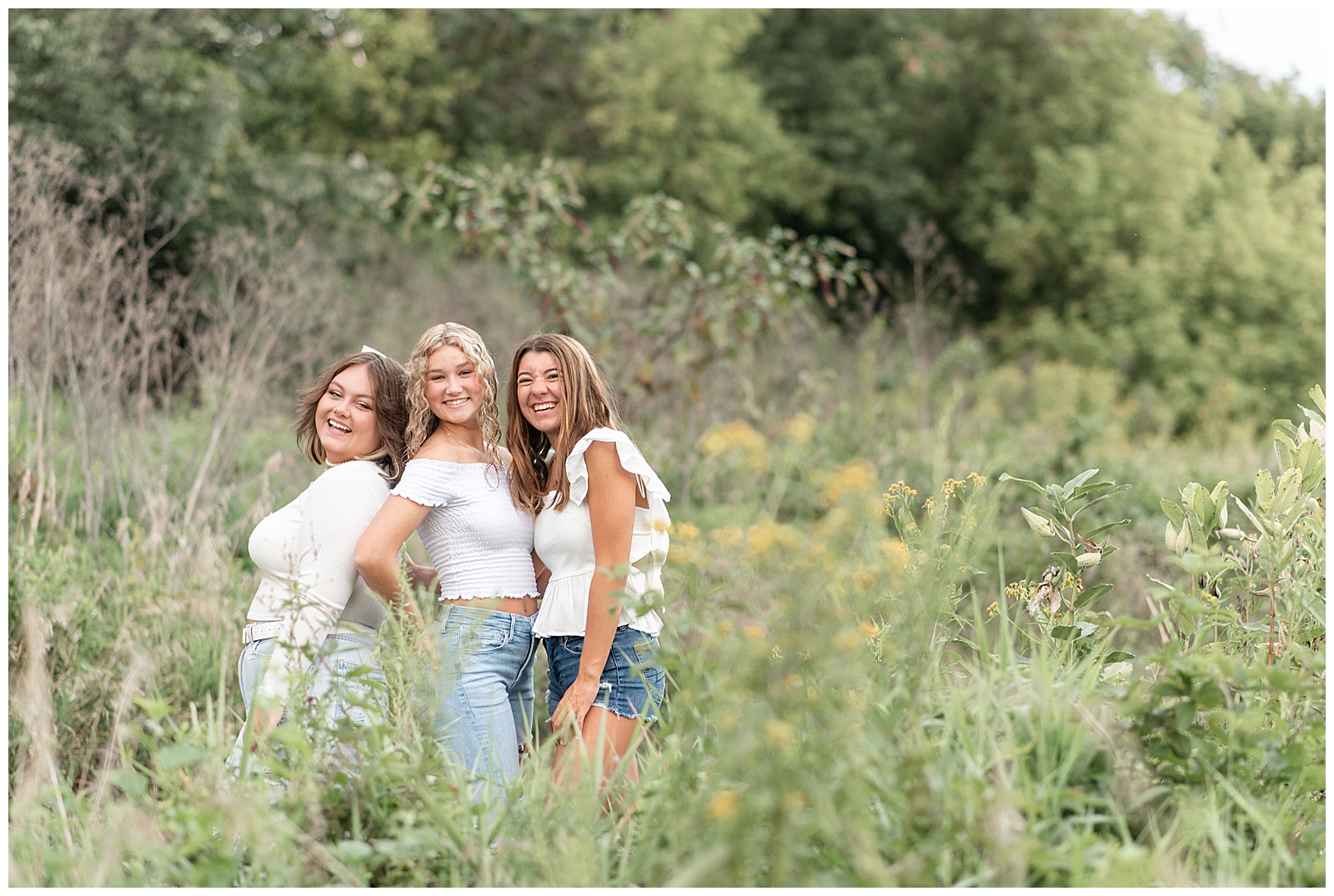 three senior girls standing close together in field of tall wild grasses and flowers at sunset at lancaster county central park