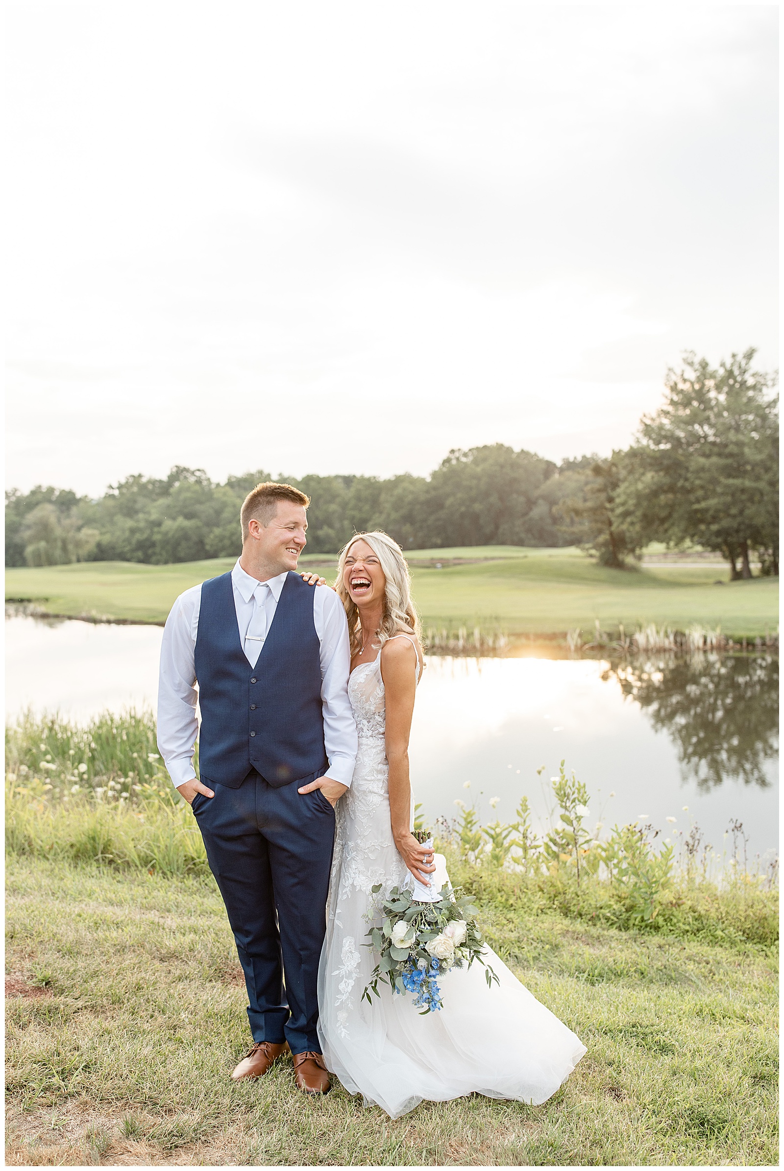 bride laughing big as she holds onto her groom's left arm by pond at the links at gettysburg at sunset