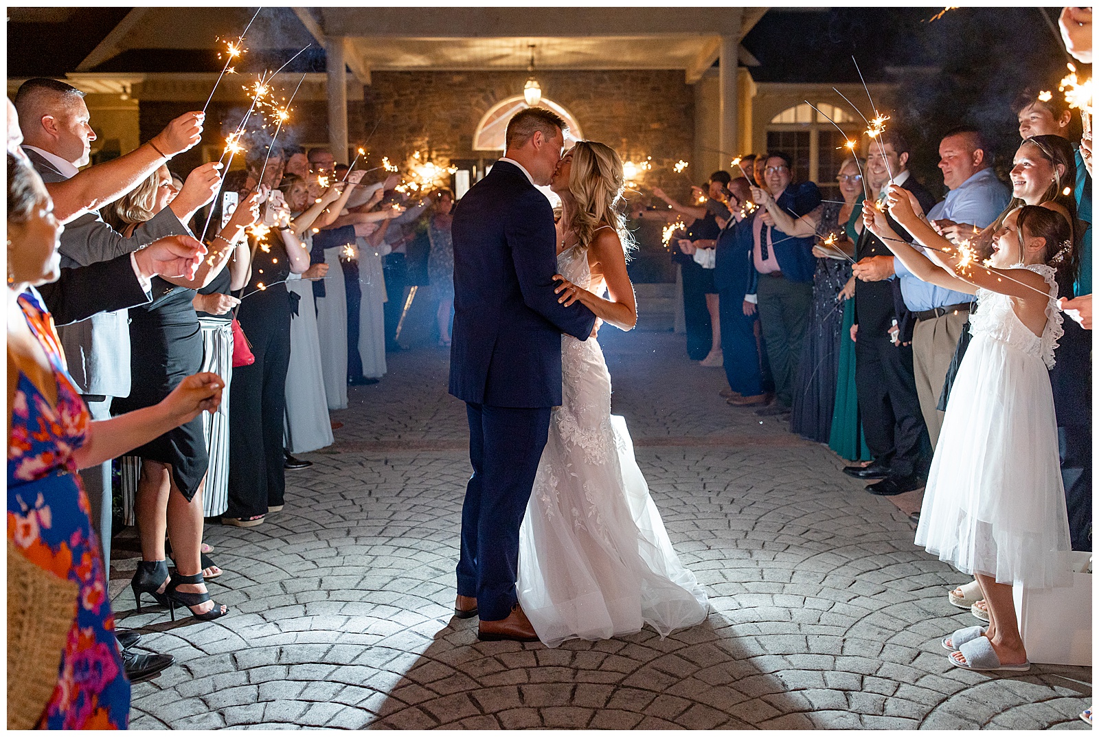 couple sharing a kiss as they exit their wedding reception in an aisle of their guests holding sparklers at nighttime in gettysburg pa