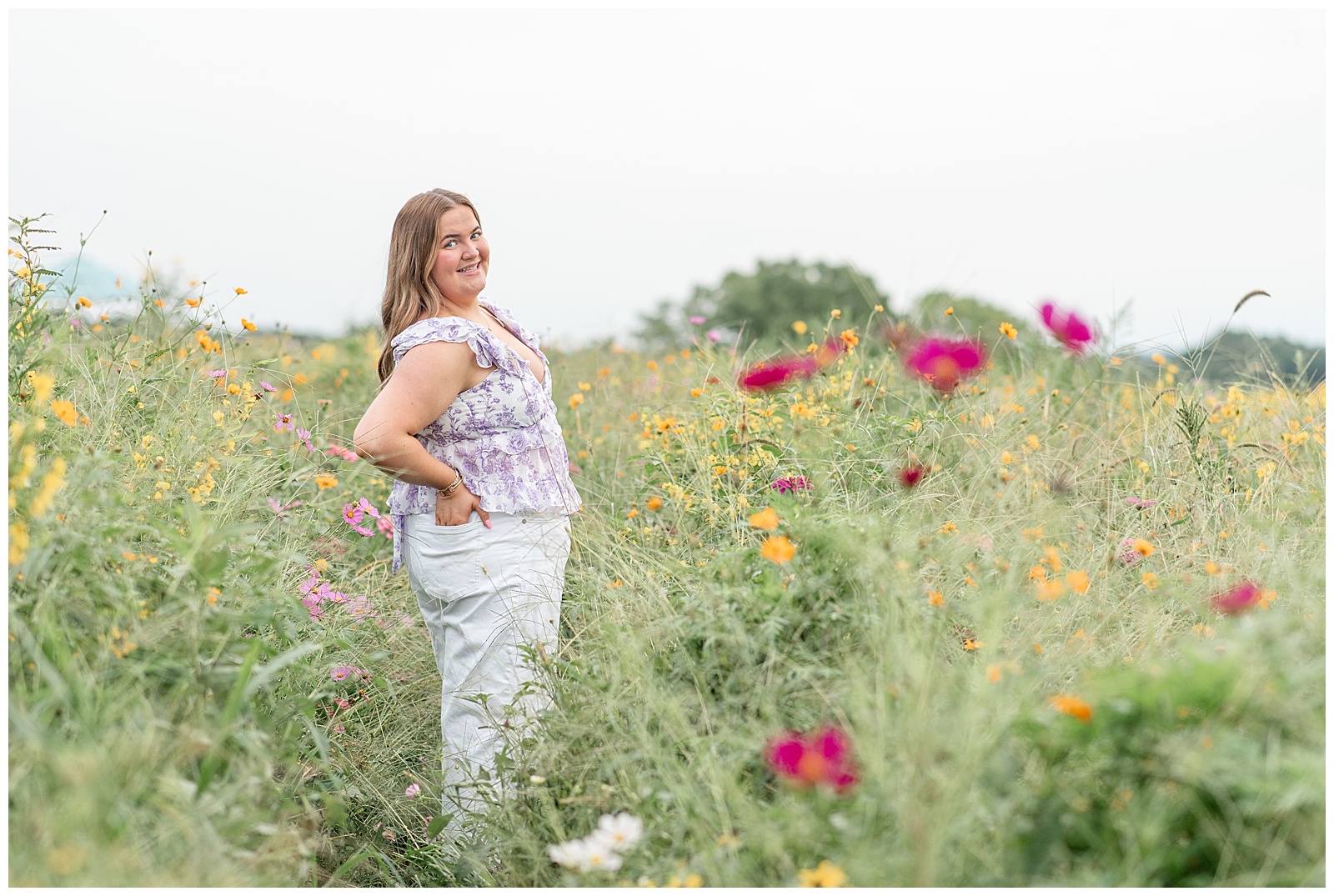 senior girl with her right hand on hip looking back at camera for this Cloudy Wildflower Field Senior Session