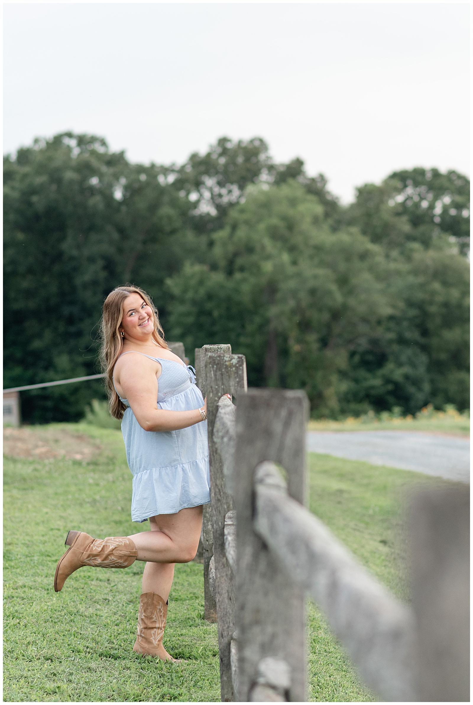 senior girl holding onto wooden fence and kicking up her right footed cowboy boot in lancaster pennsylvania