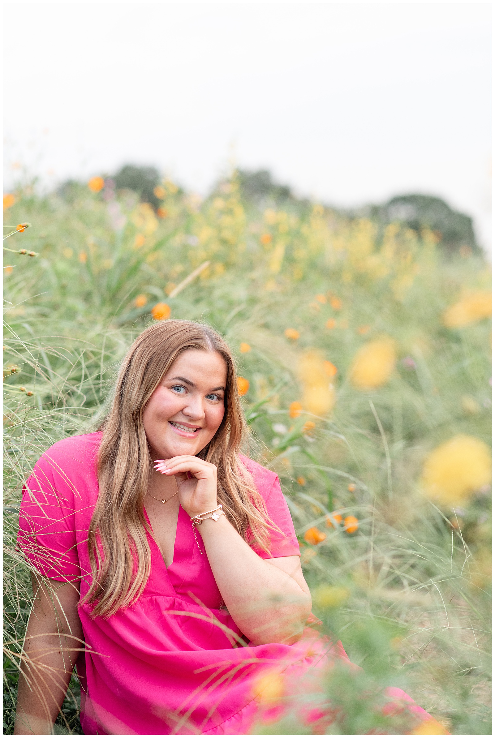 senior girl resting chin on left hand sitting on the ground for this Cloudy Wildflower Field Senior Session