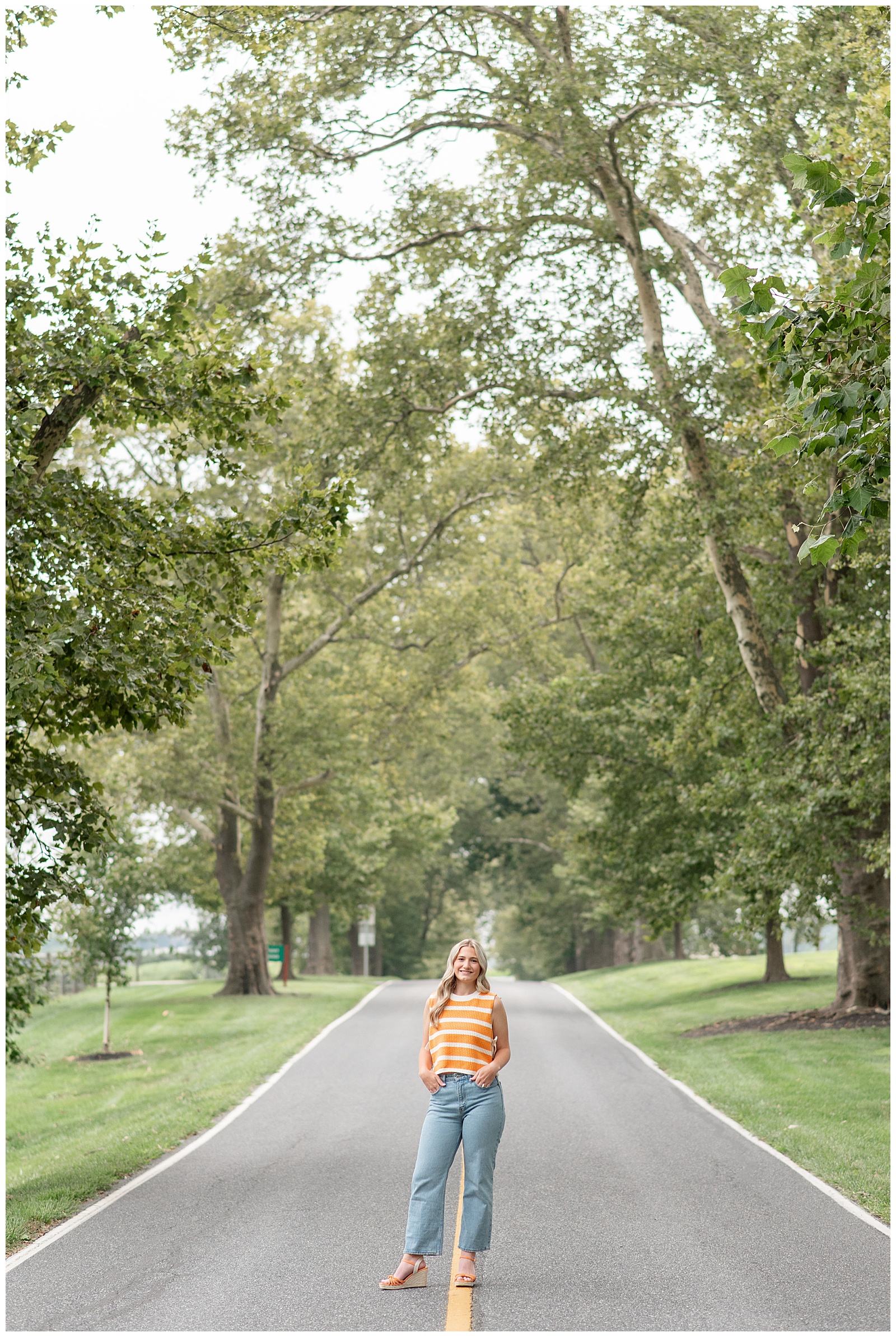 senior girl in yellow and white striped shirt and blue jeans standing in middle of road for this Masonic Village Summer Senior Session