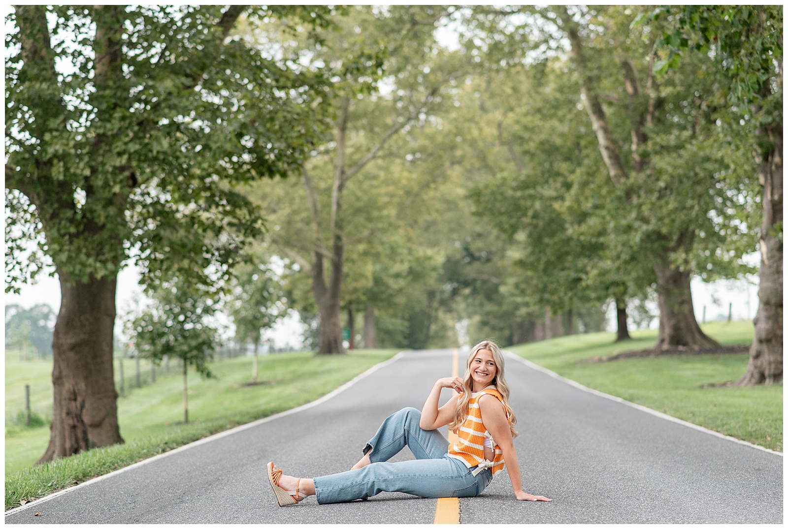 senior girl sitting in middle of street with left leg extended and right knee bent for this Masonic Village Summer Senior Session
