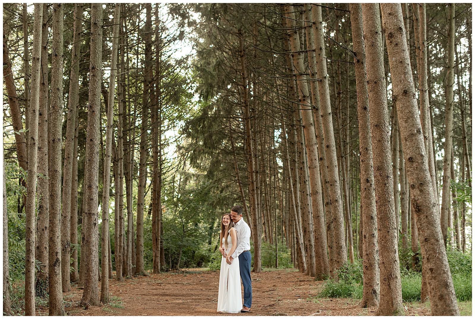 man standing behind woman in between rows of evergreen trees for this Fall Overlook Park Engagement Session