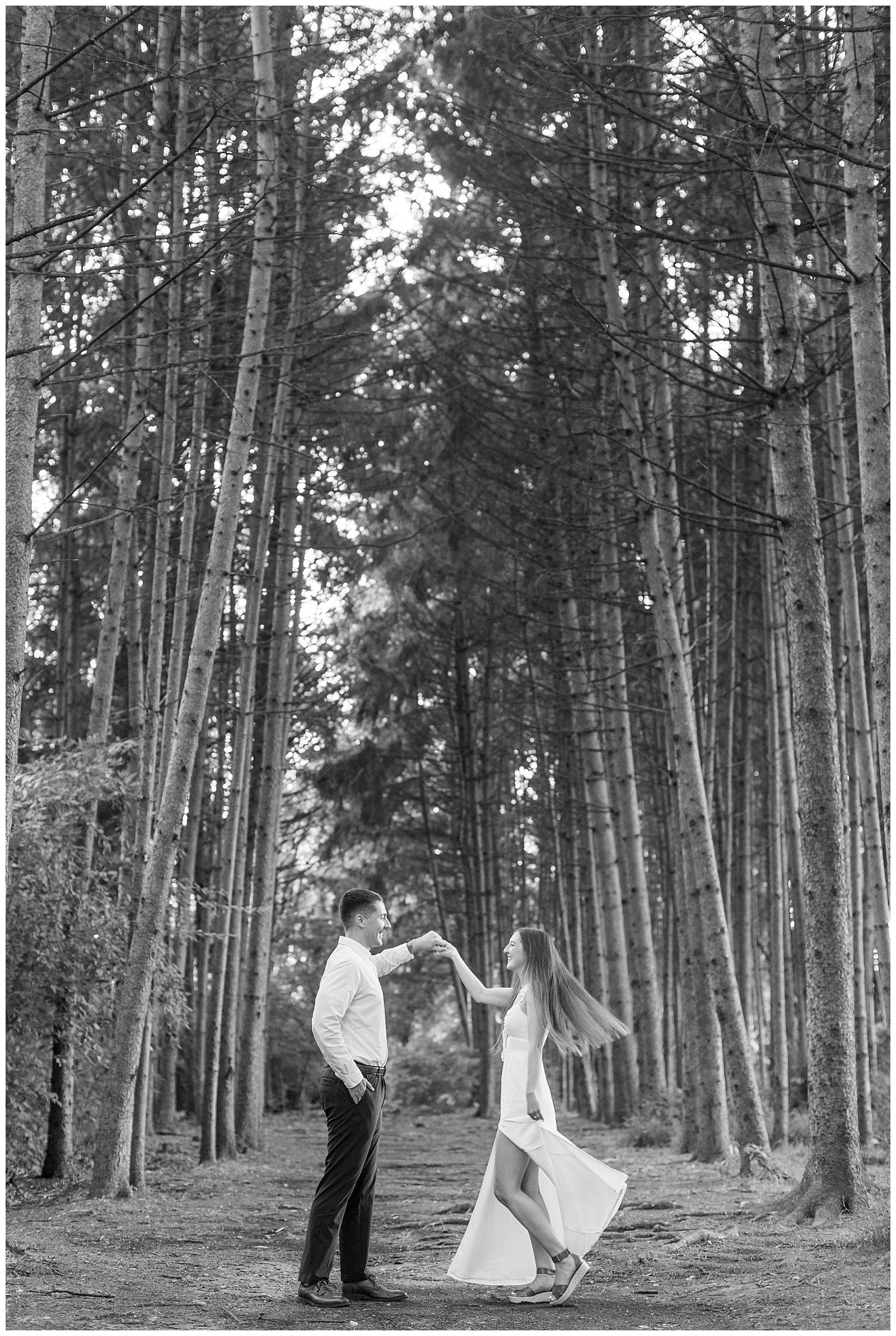 black and white photo of guy twirling girl in forest of evergreen trees for this Fall Overlook Park Engagement Session