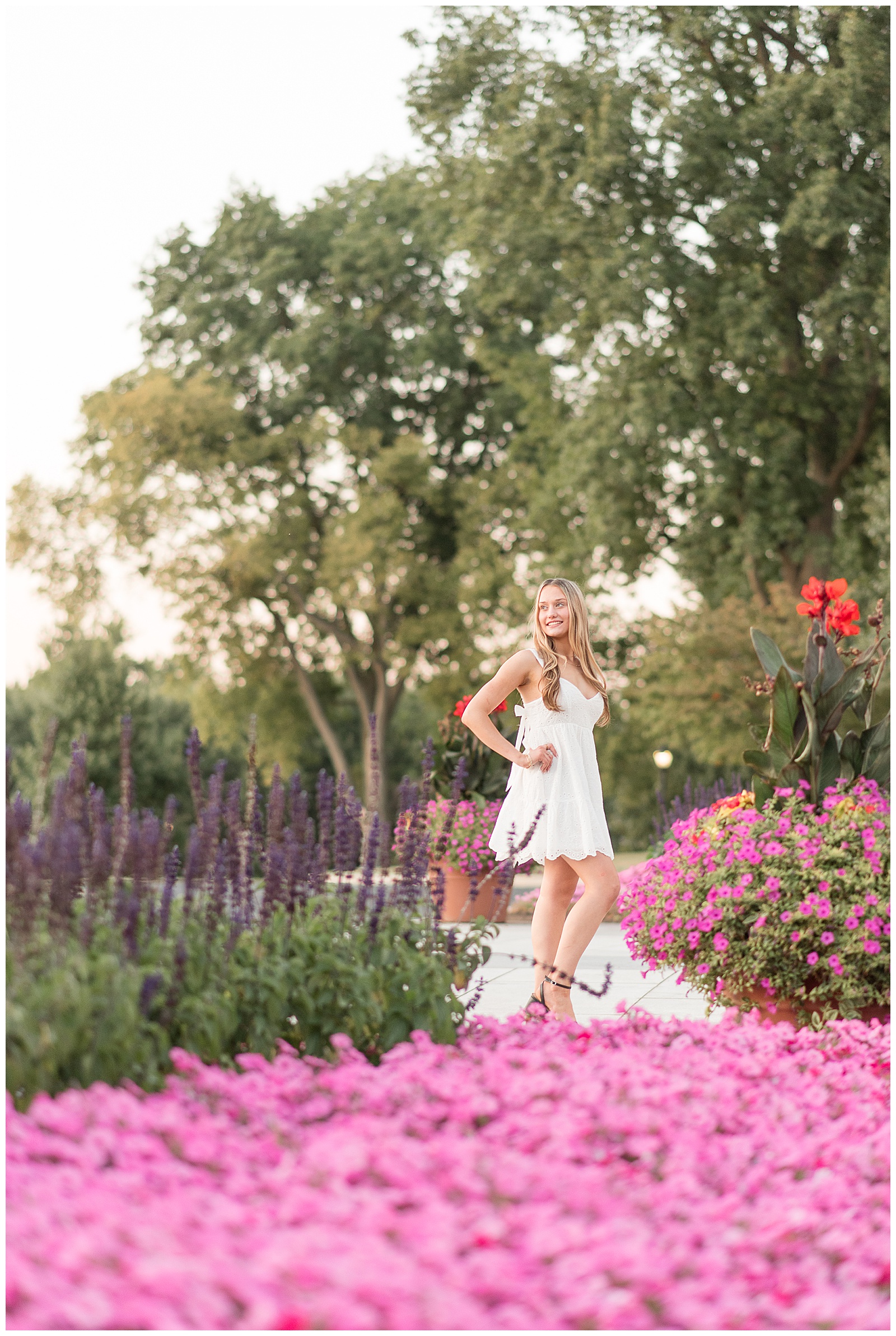 senior girl standing on path filled with colorful flowers with right hand on hip for this Founders Hall Summer Senior Session