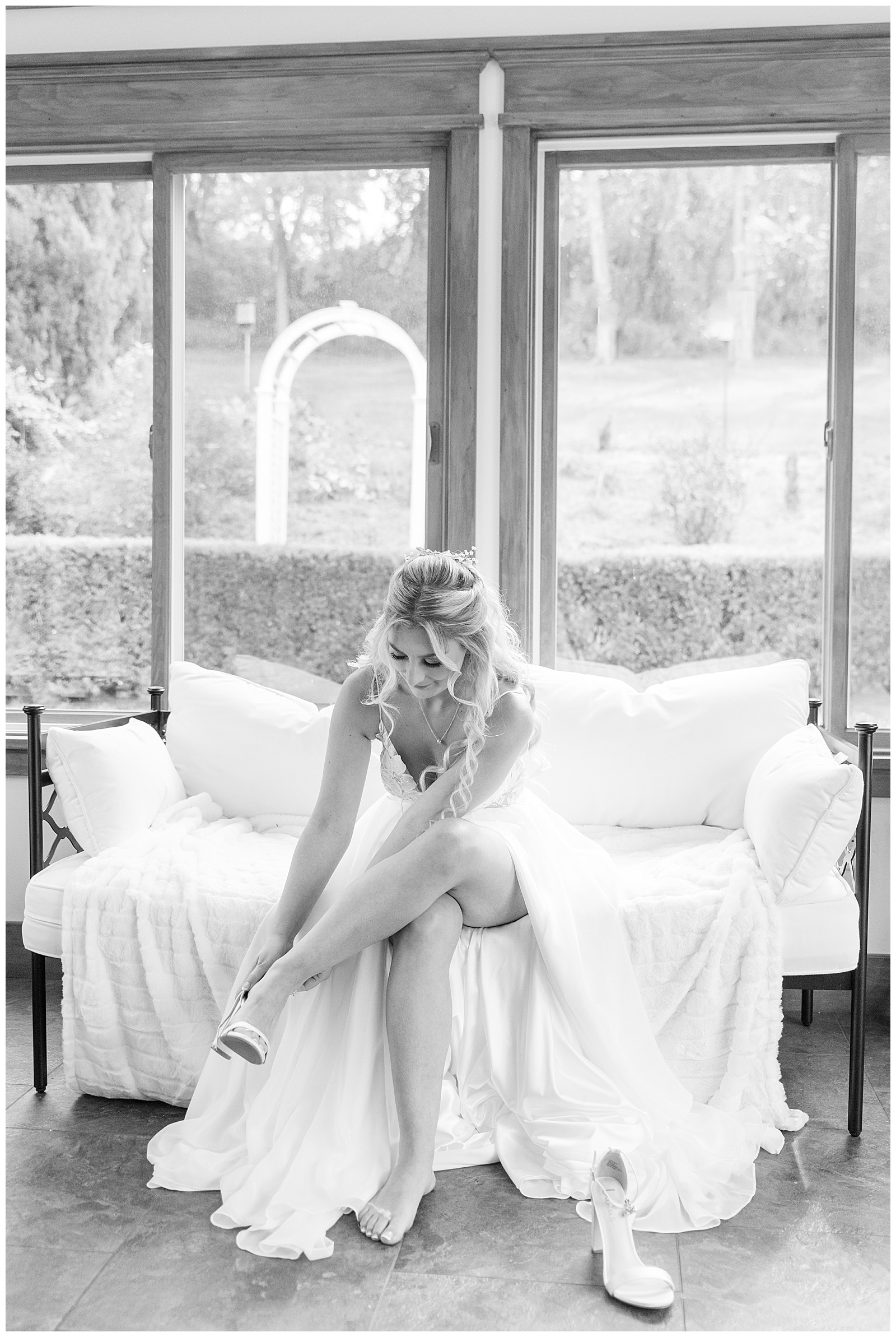 black and white photo of bride in gown putting on shoes inside sunroom for this Central PA Farm Wedding