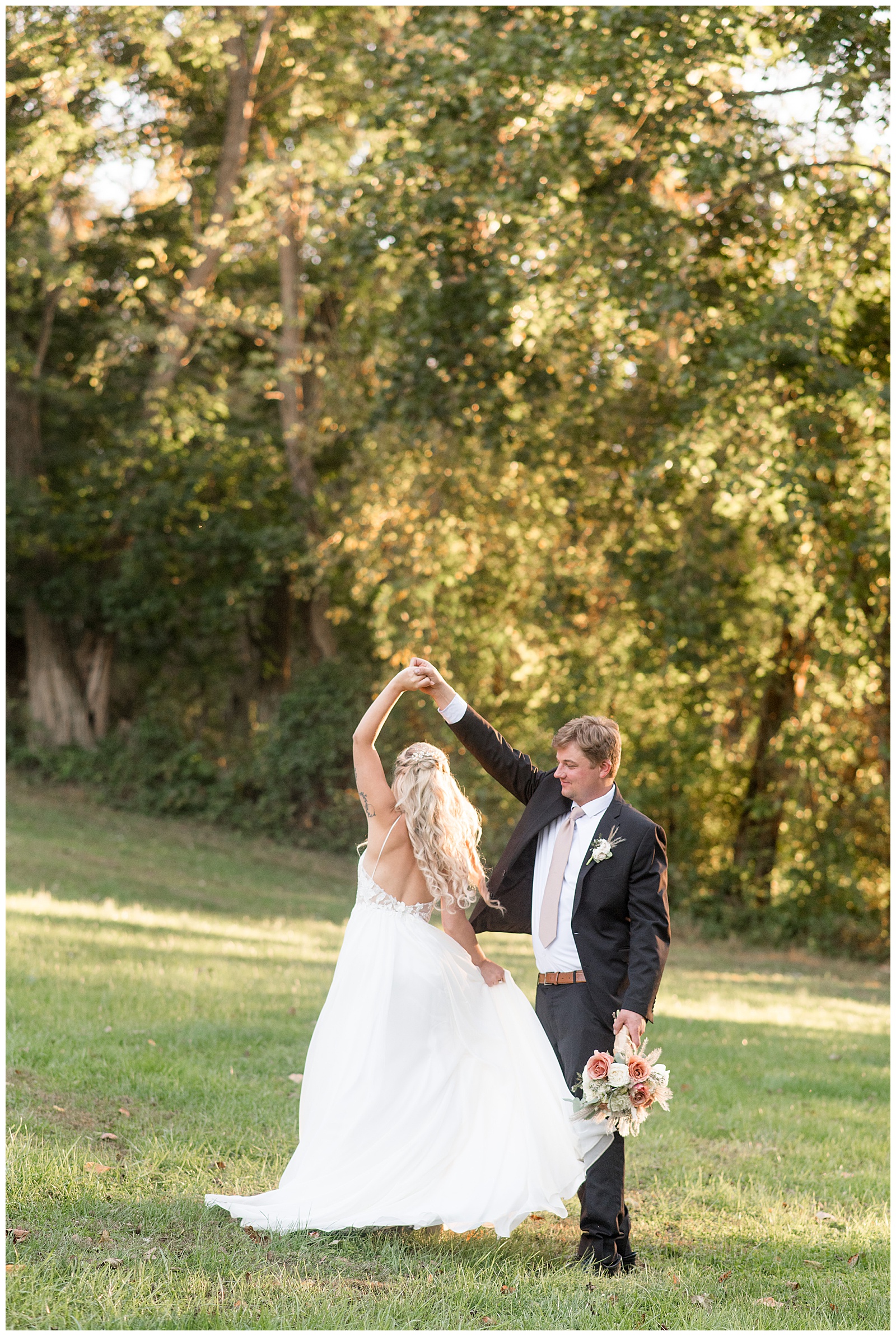 groom holding bride's bouquet and twirling her under his right hand for this Central PA Farm Wedding