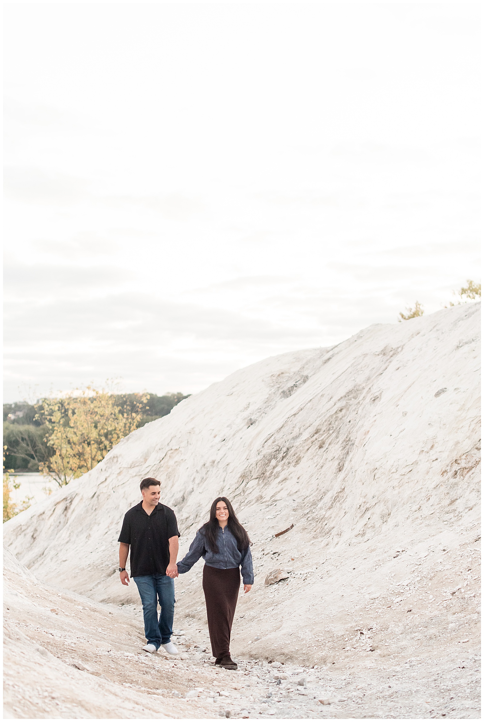 couple holding hands and walking towards camera by white mountain for this White Cliffs of Conoy Fall Couples Session