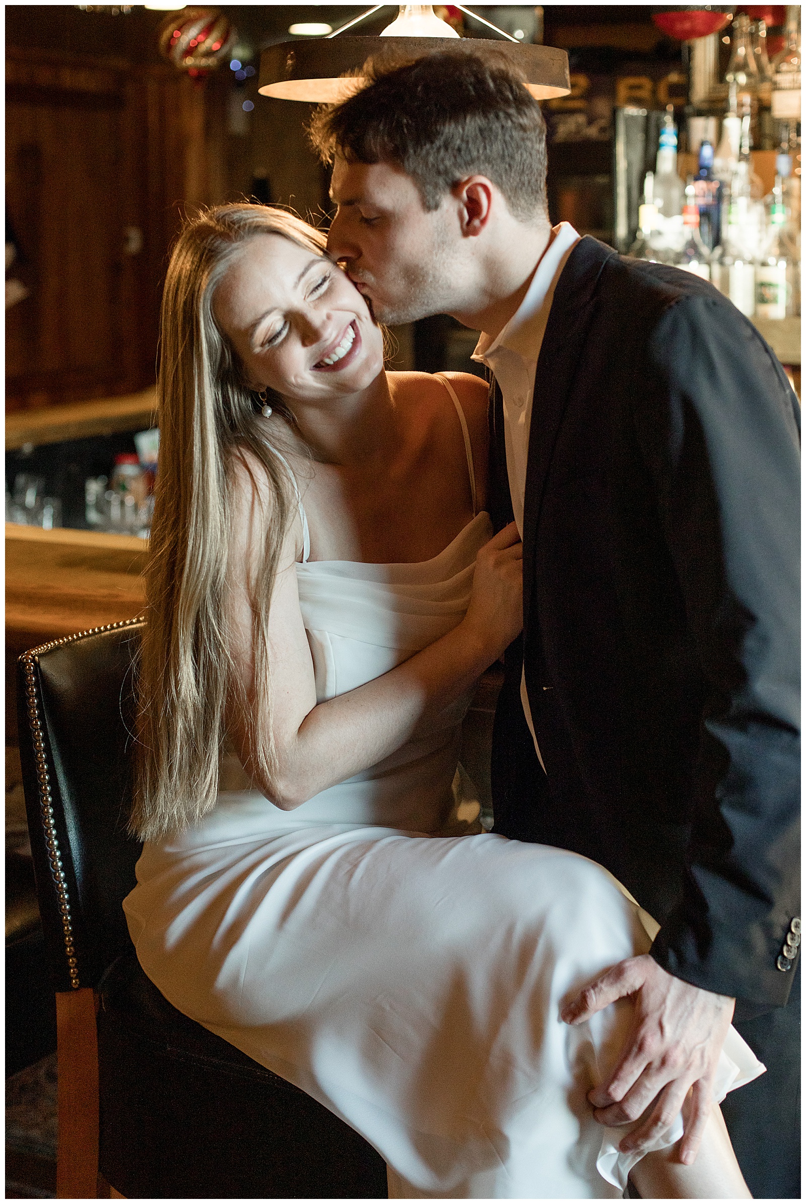 guy kissing girl's left cheek as she smiles big at bar for this Fells Point Engagement Session