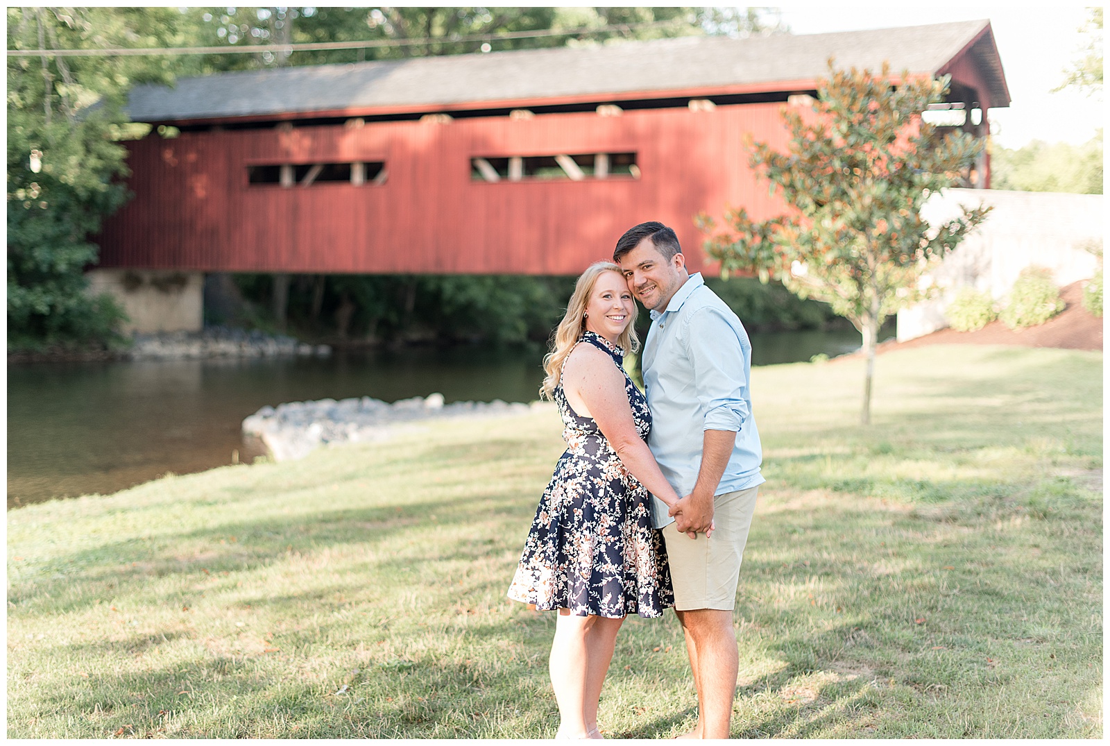 couple holding hands at side smiling at camera in front of red bridge at Messiah College