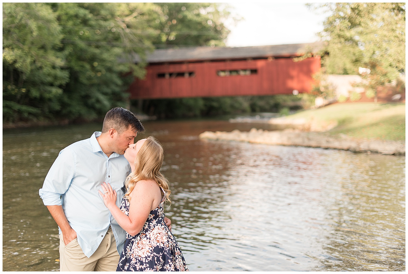 couple standing in water kissing in front of red bridge at Messiah College