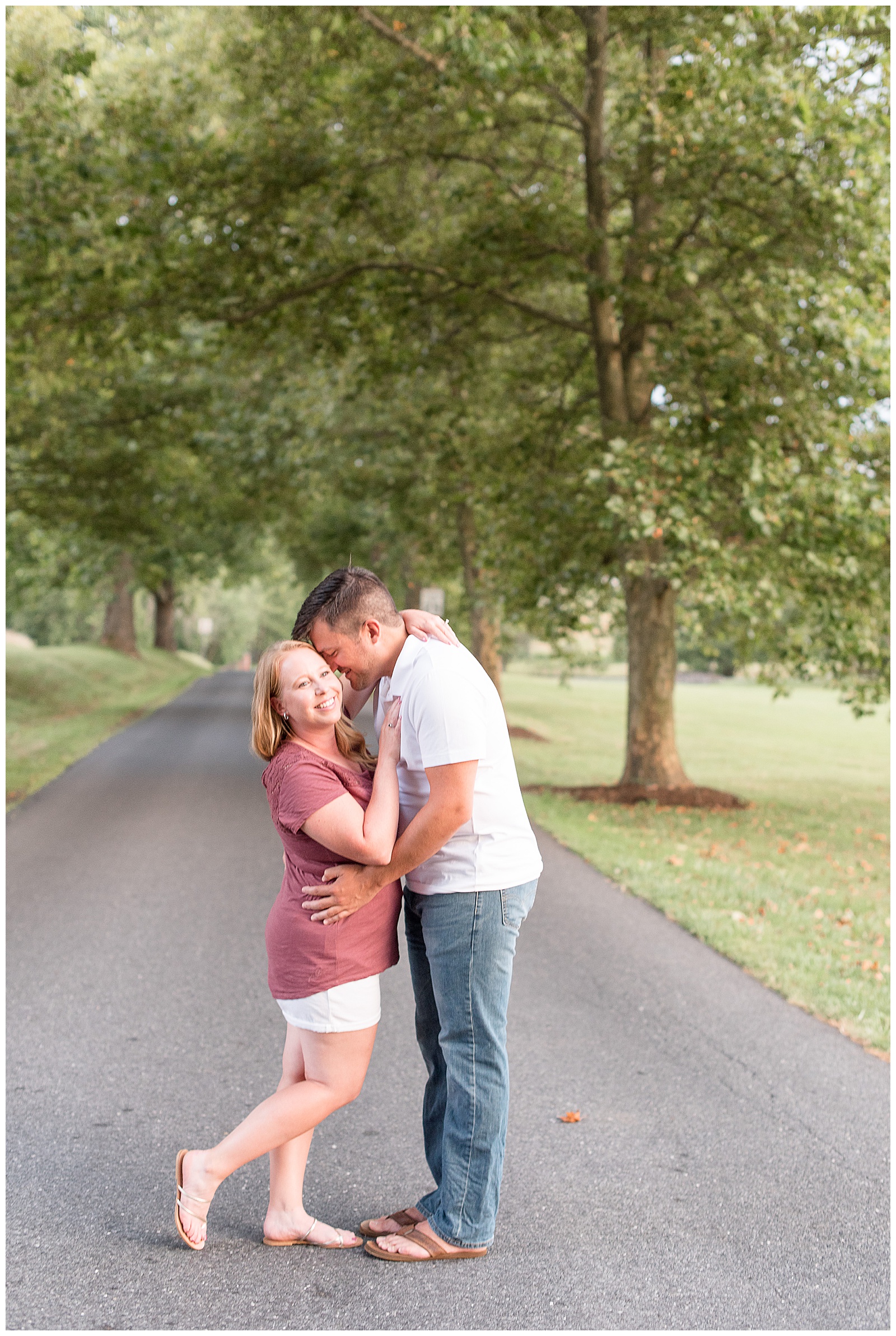 guy kissing girl on cheek in middle of road that is lined with trees