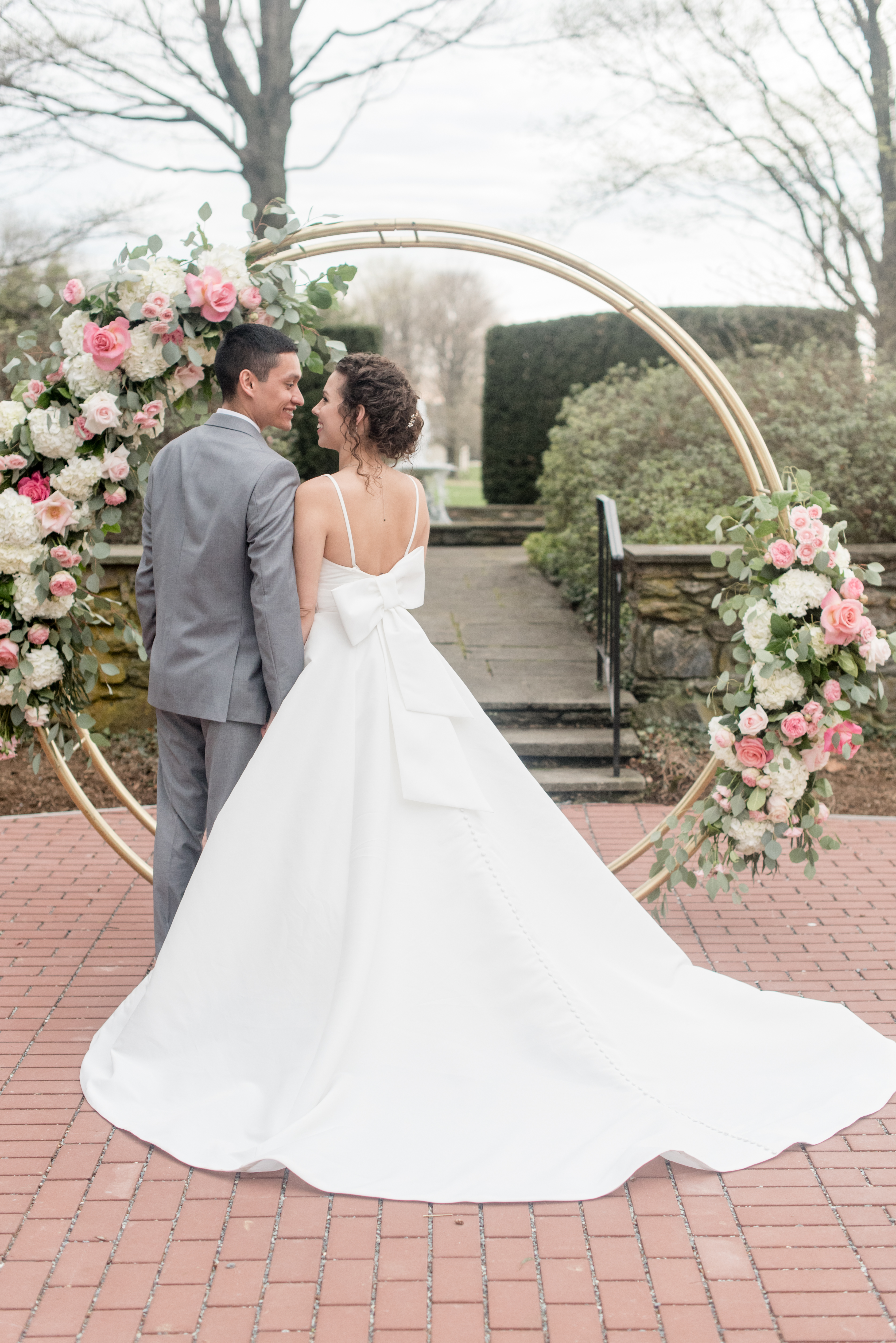 bride and groom standing in front of a circular arbor with florals on it