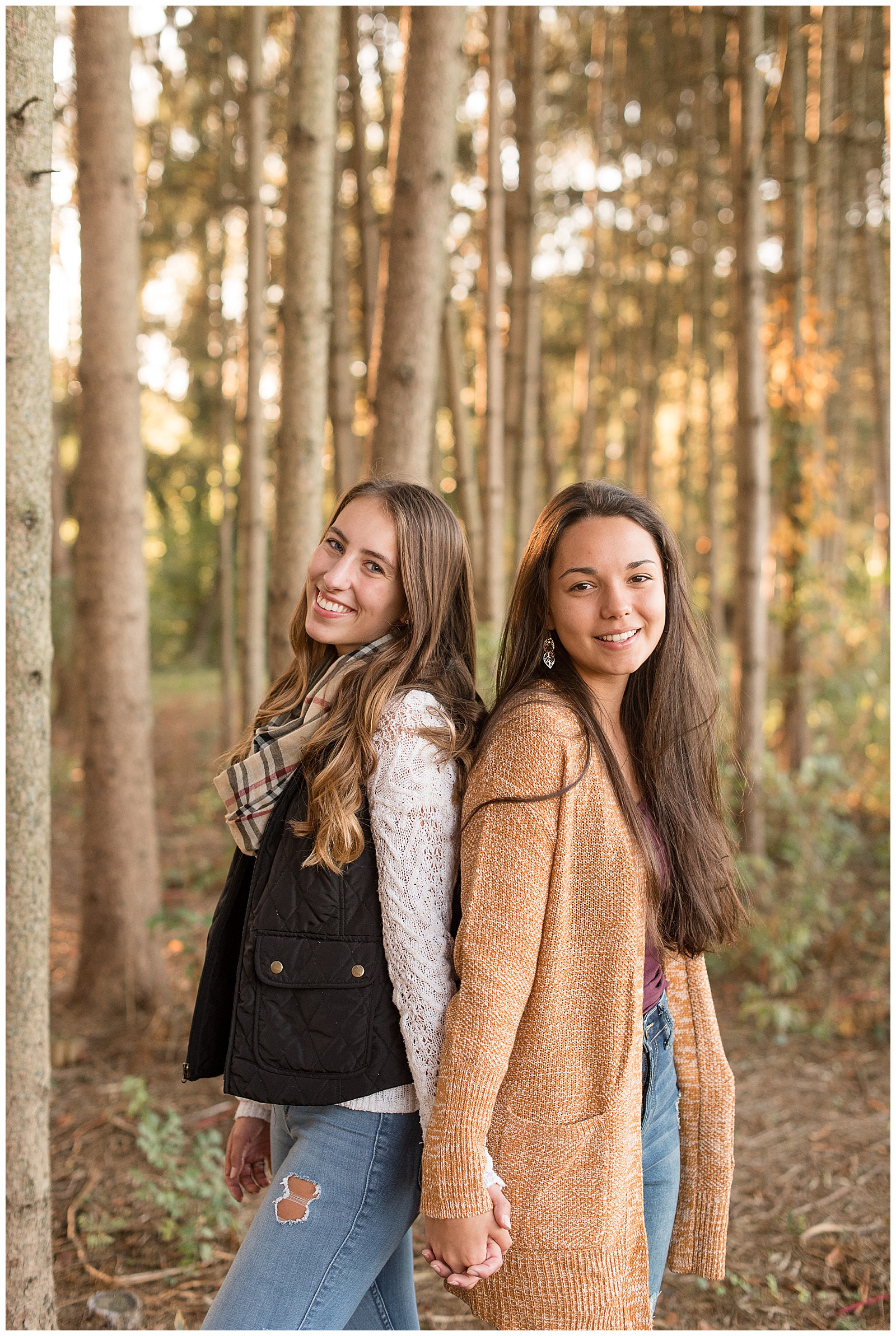 fall senior session of two girls holding hands with backs against each other