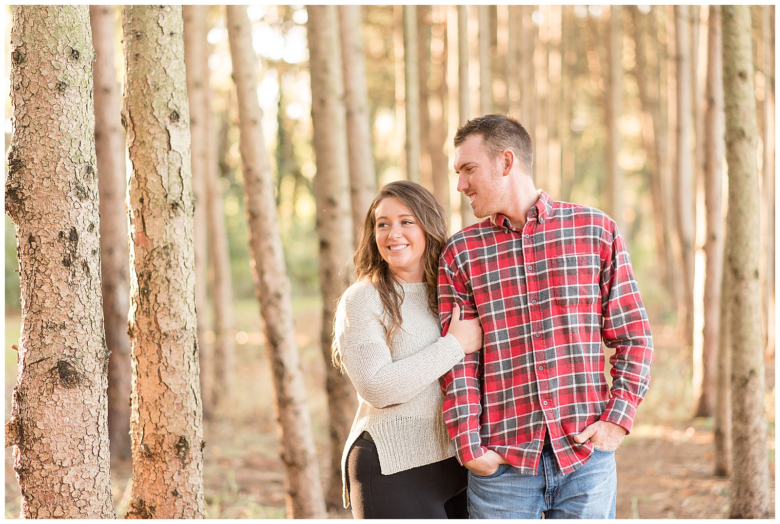 couple amongst a forest of pine trees with sun shining in from behind