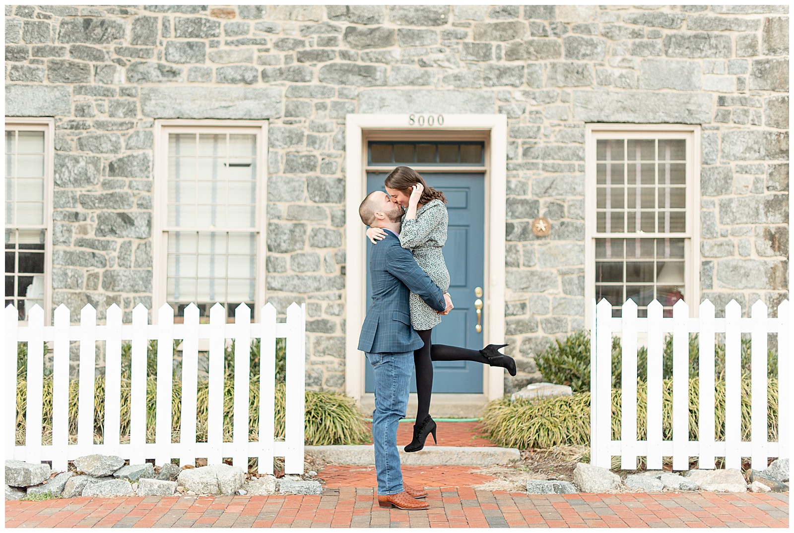 guy lifting girl up as they share a kiss in front of a stone home