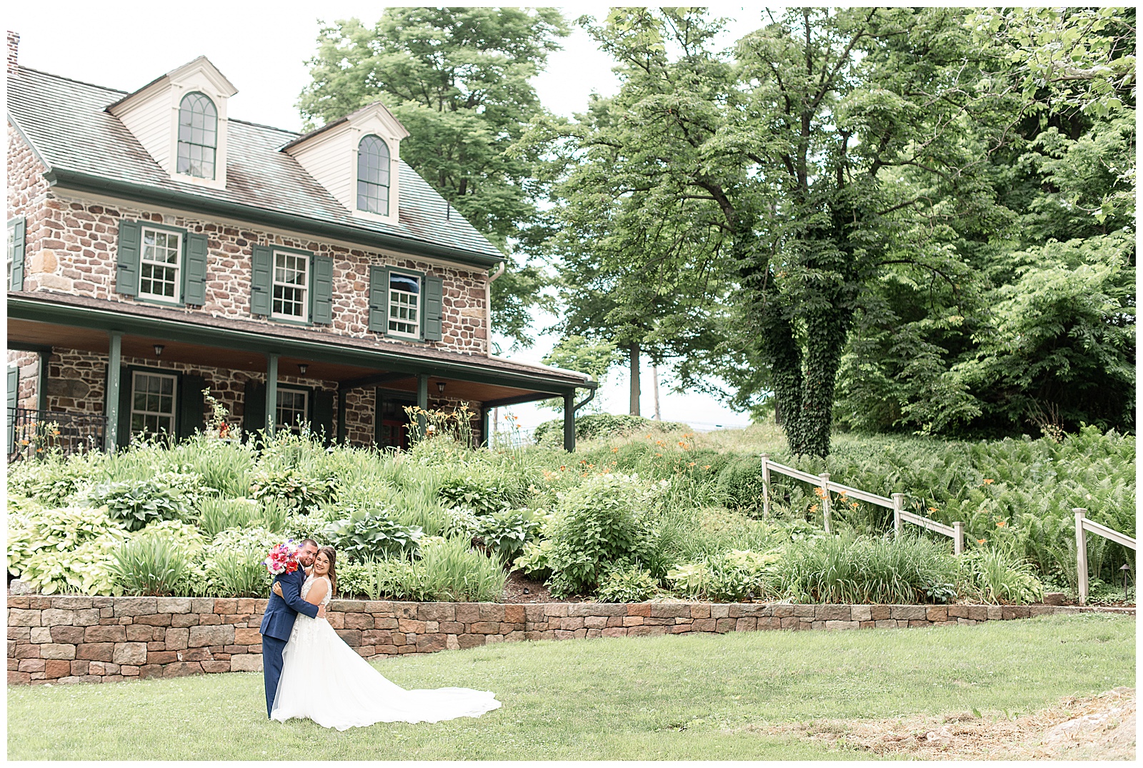 bride and groom portraits with groom dipping bride in front of stone house