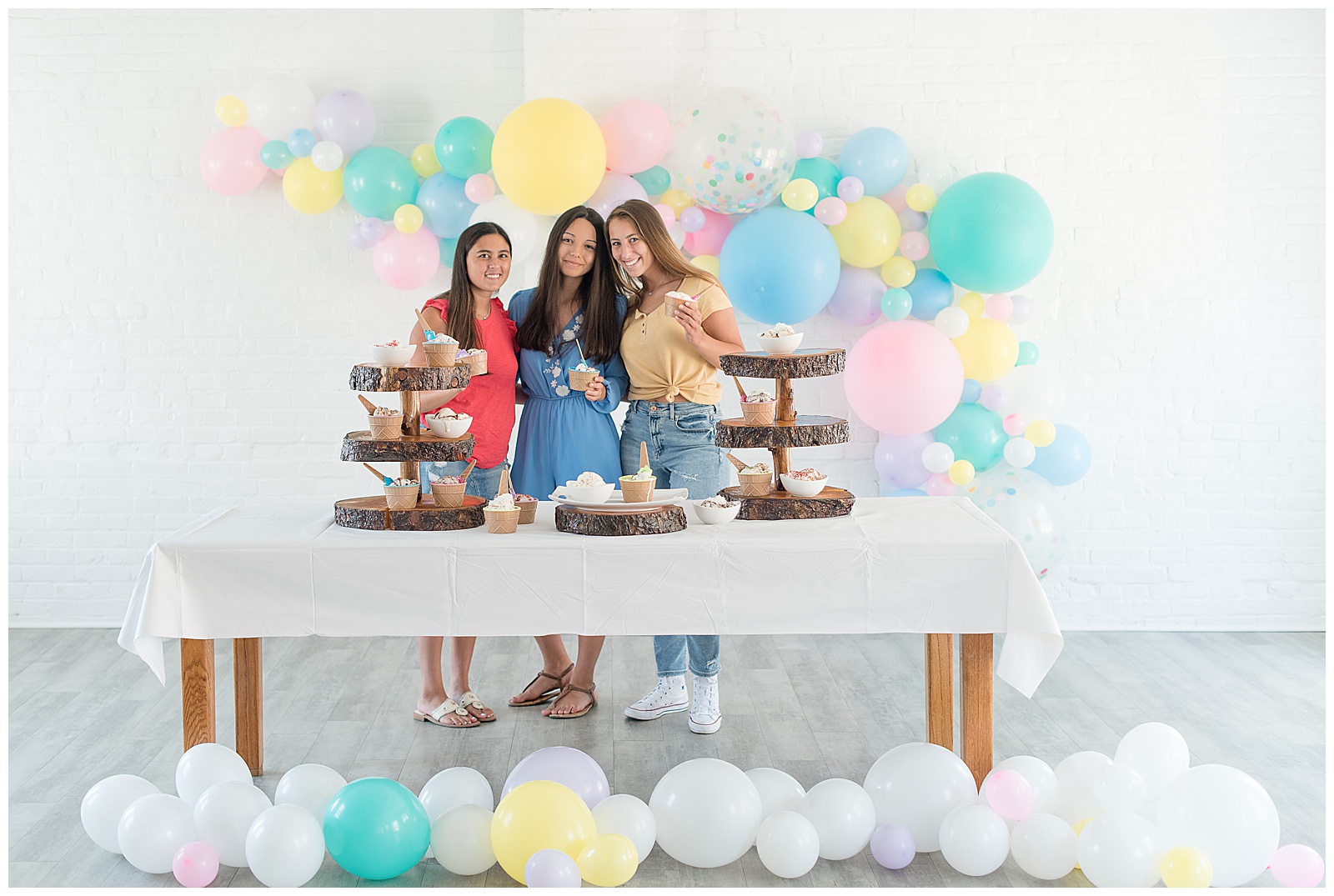 senior spokesmodels standing behind table of ice cream with ballons hanging on wall behind