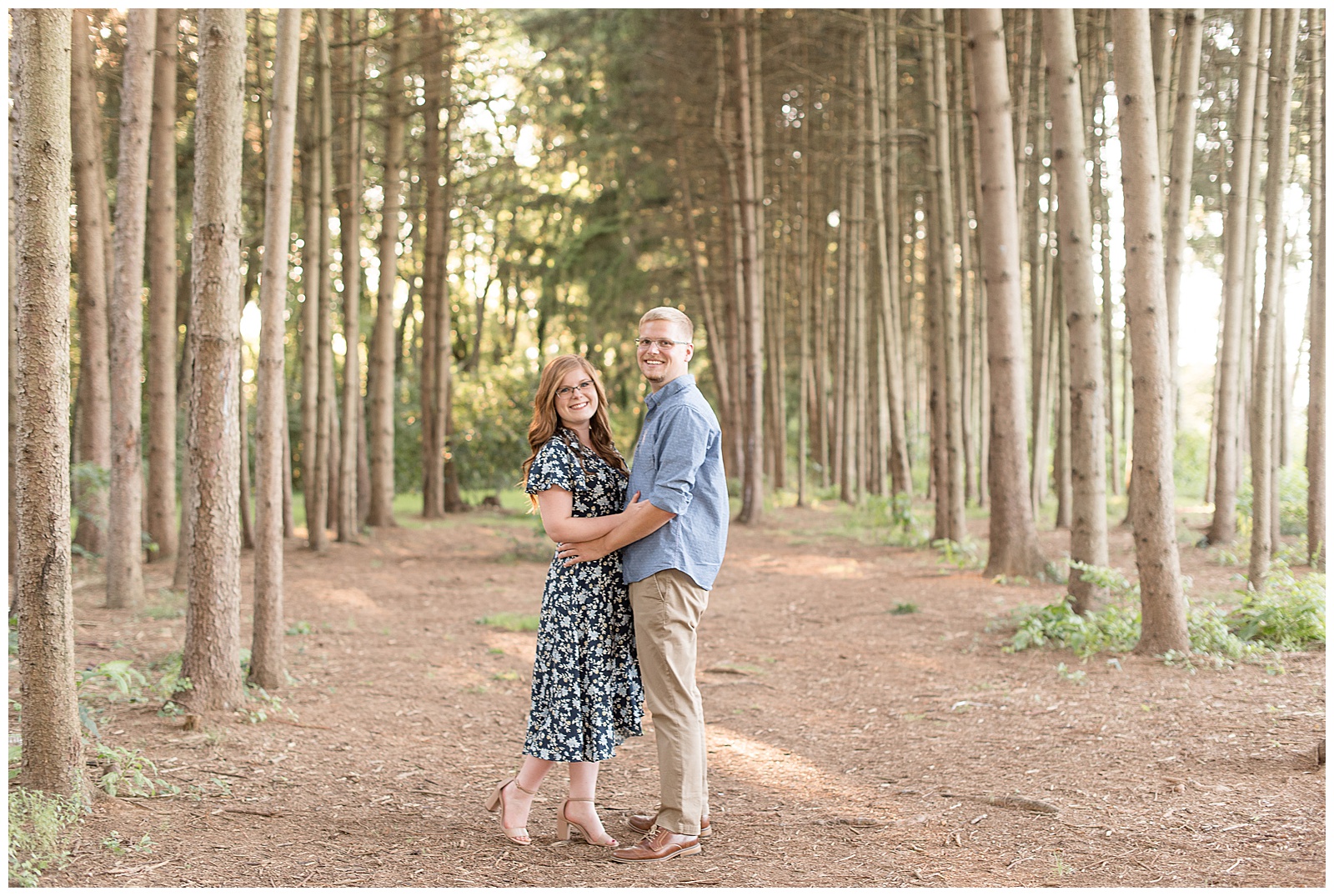 coupld facing each other and smiling towards camera with arms wrapped around each other surrounded by a grove of pine trees in Lancaster, PA
