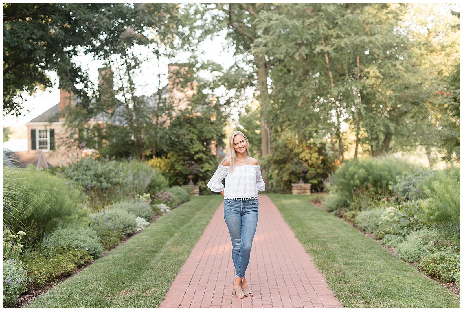 2021 Senior Session at Drumore Estate with senior standing on brick path with hands in pockets and ankles crossed, smiling at camera