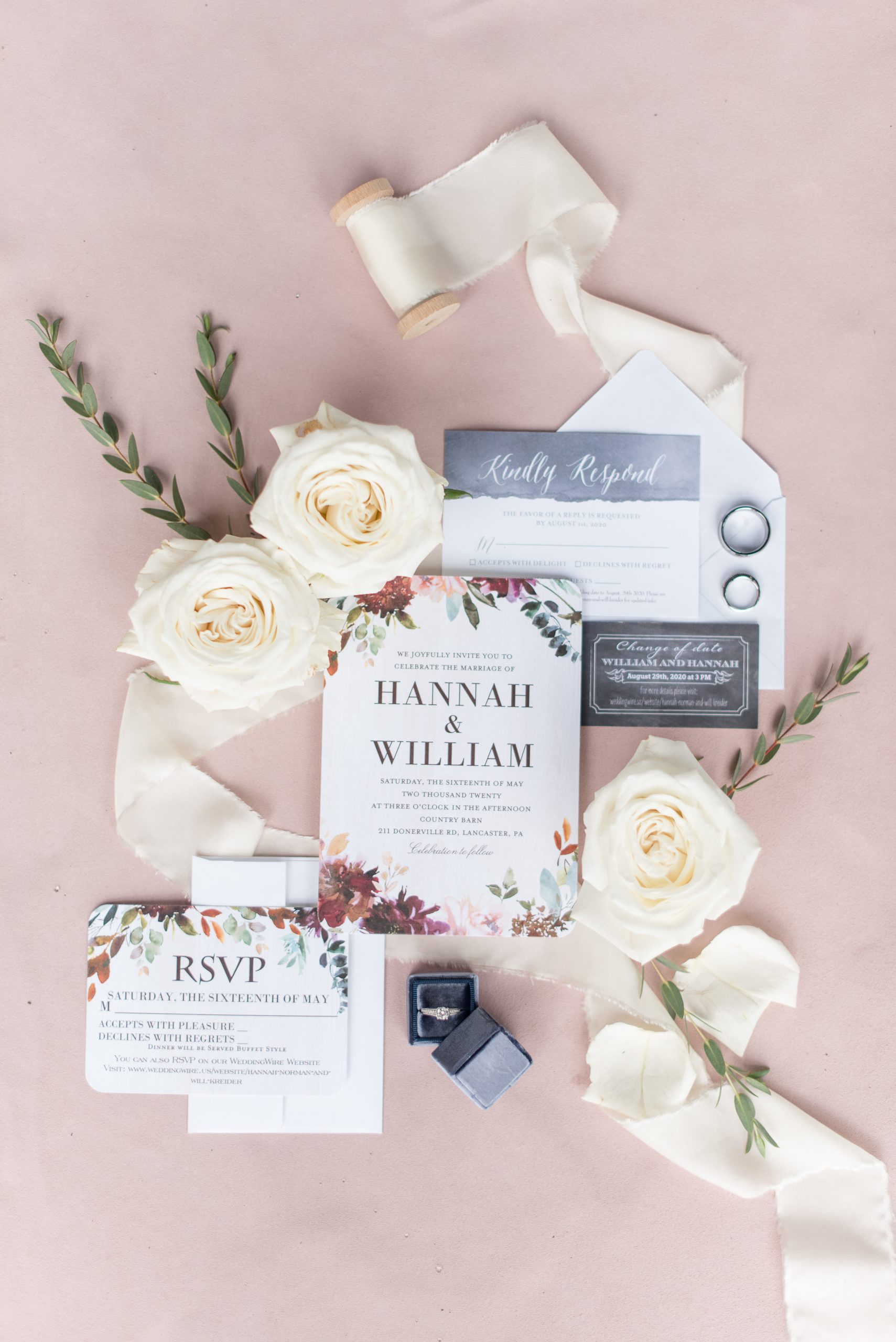 wedding details flat lay of invitation suite, white florals, and wedding rings on suede background