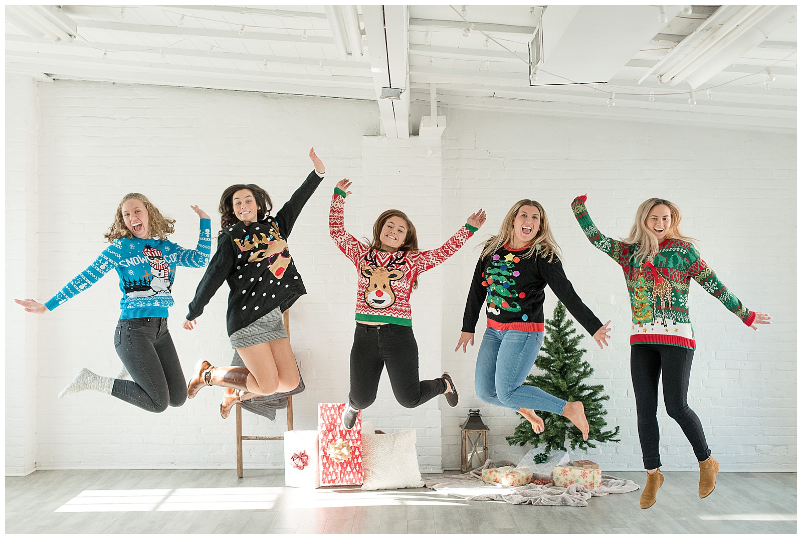 girls wearing colorful christmas sweaters all jumping with arms high and smiling at hingeworks