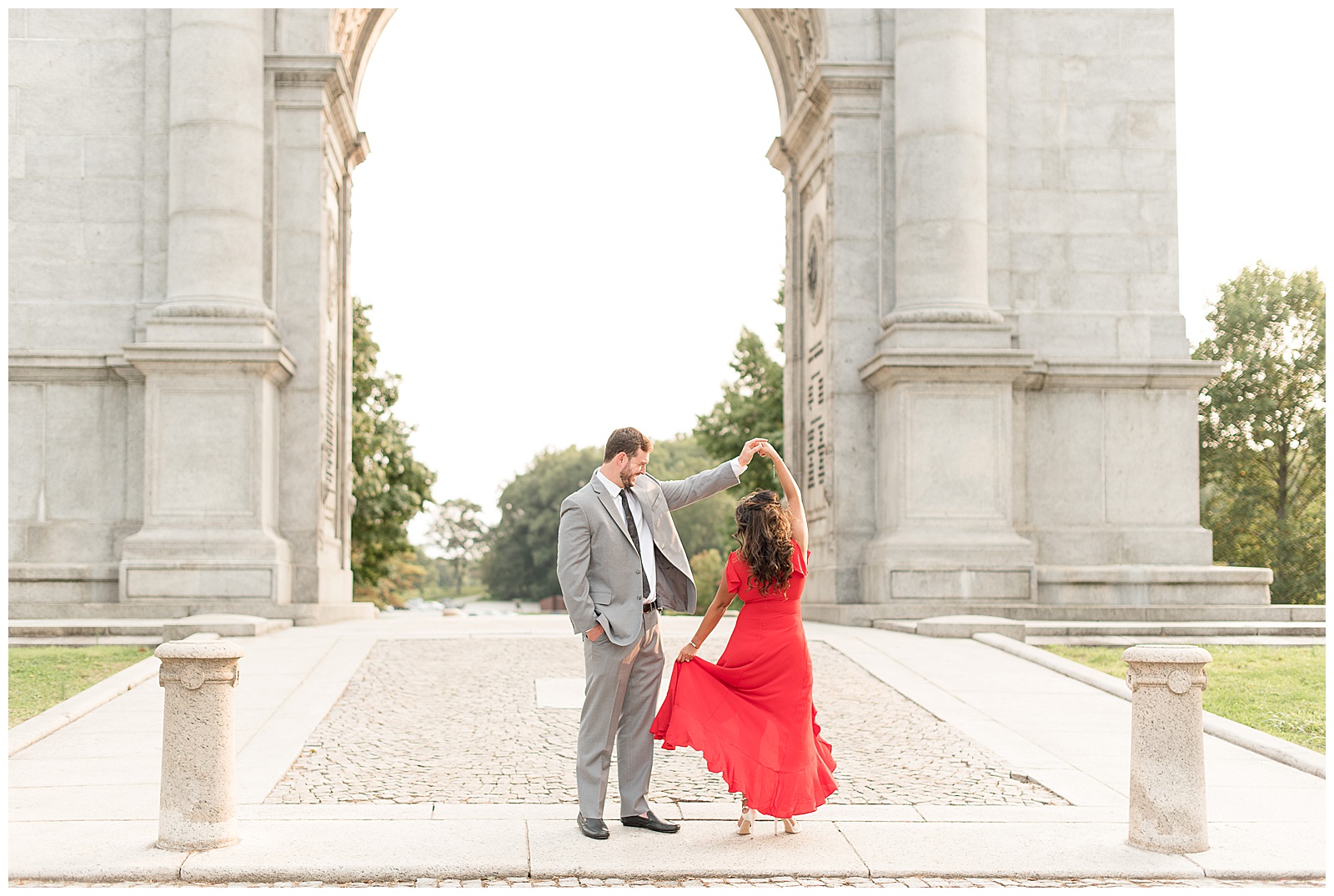 guy twirling couple in red dress in front of National Arch in Valley Forge