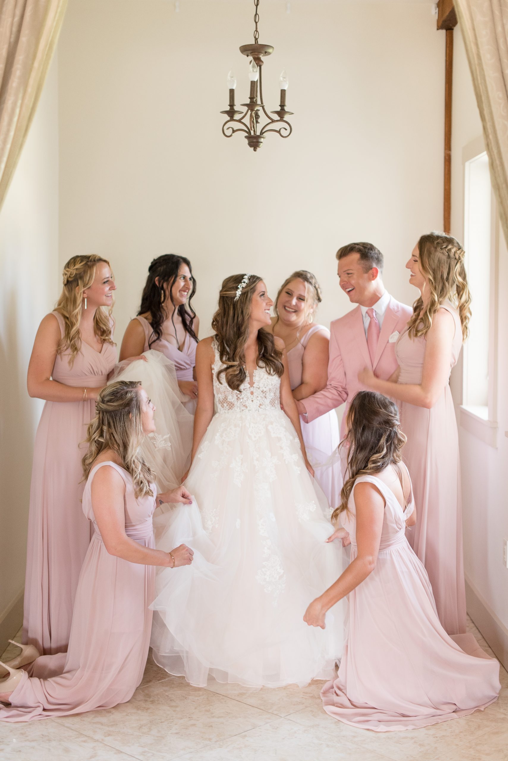bride surrounded by all her bridesmaids as they help fluff her dress.