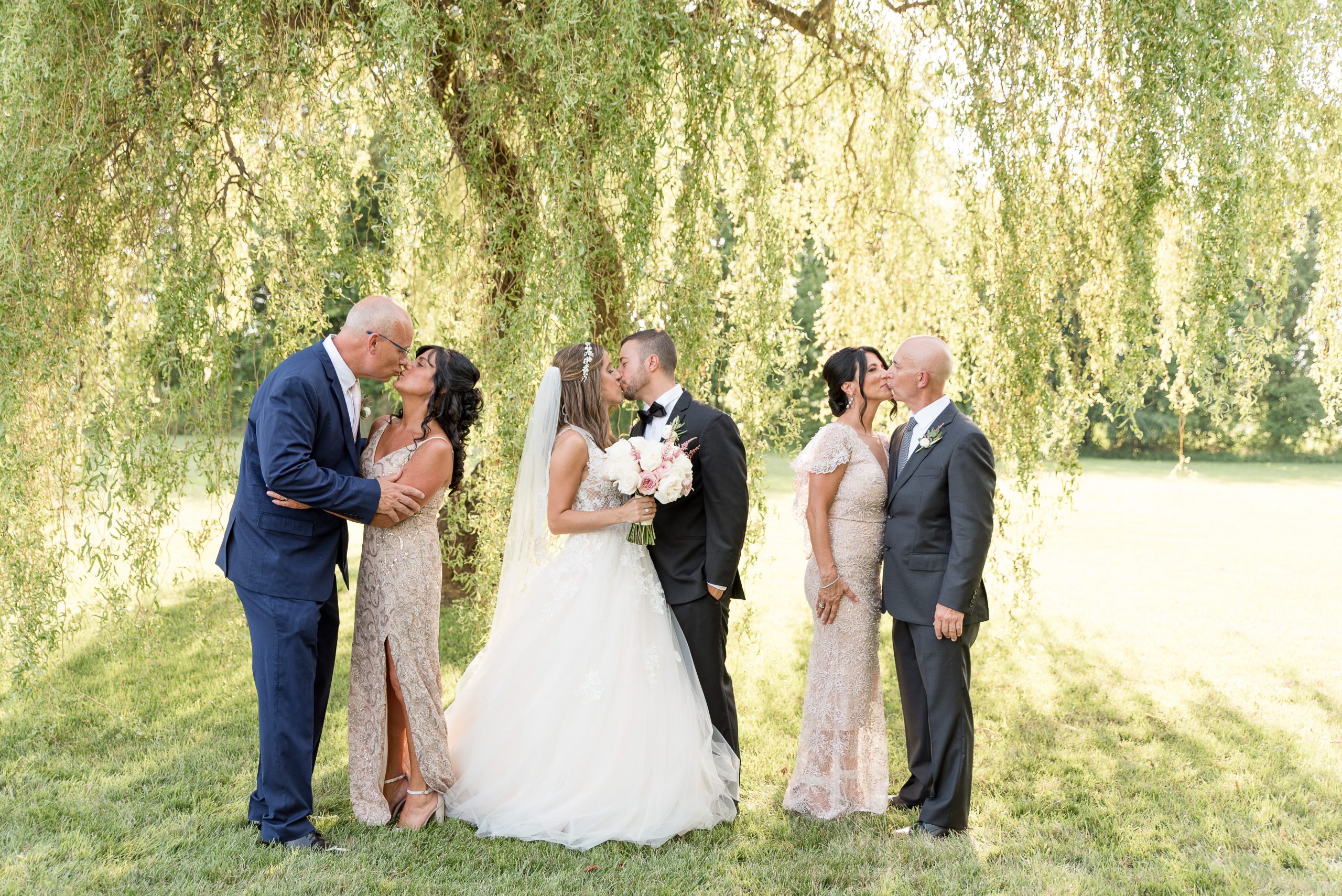 family formal of husband and wife with their parents in front of willow tree at the Barn at Silverstone