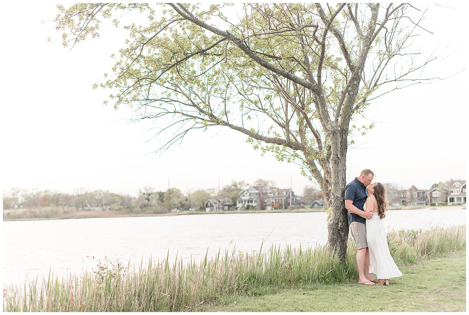 guy leans against tree as he kisses girl along the bay head harbor in new jersey on spring evening